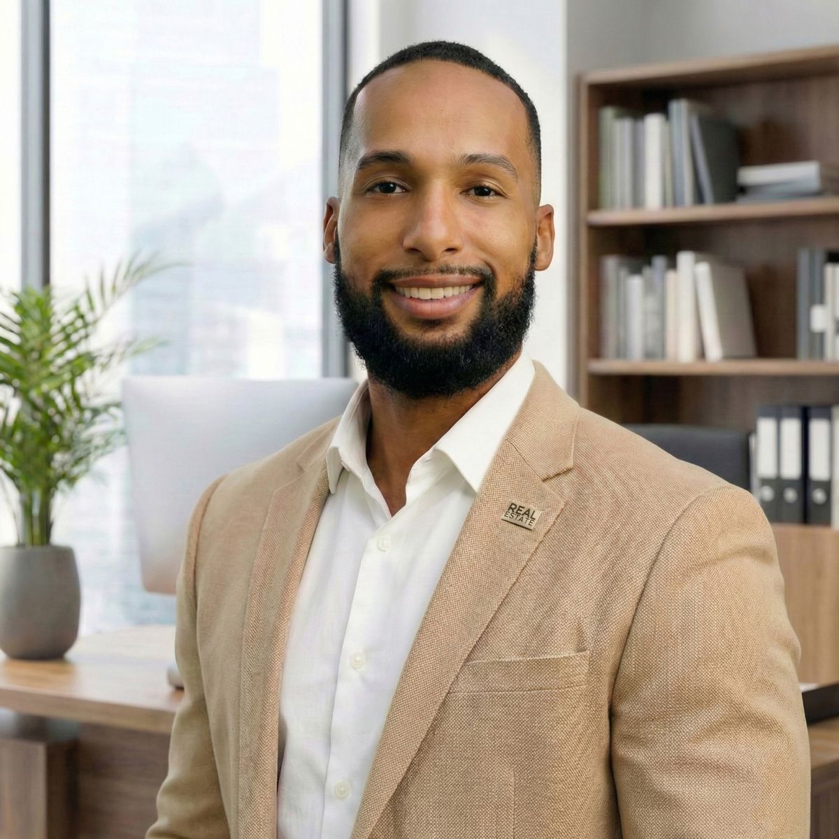 Professional wearing a beige blazer and white shirt smiles in modern office with bookshelves and plants in background.