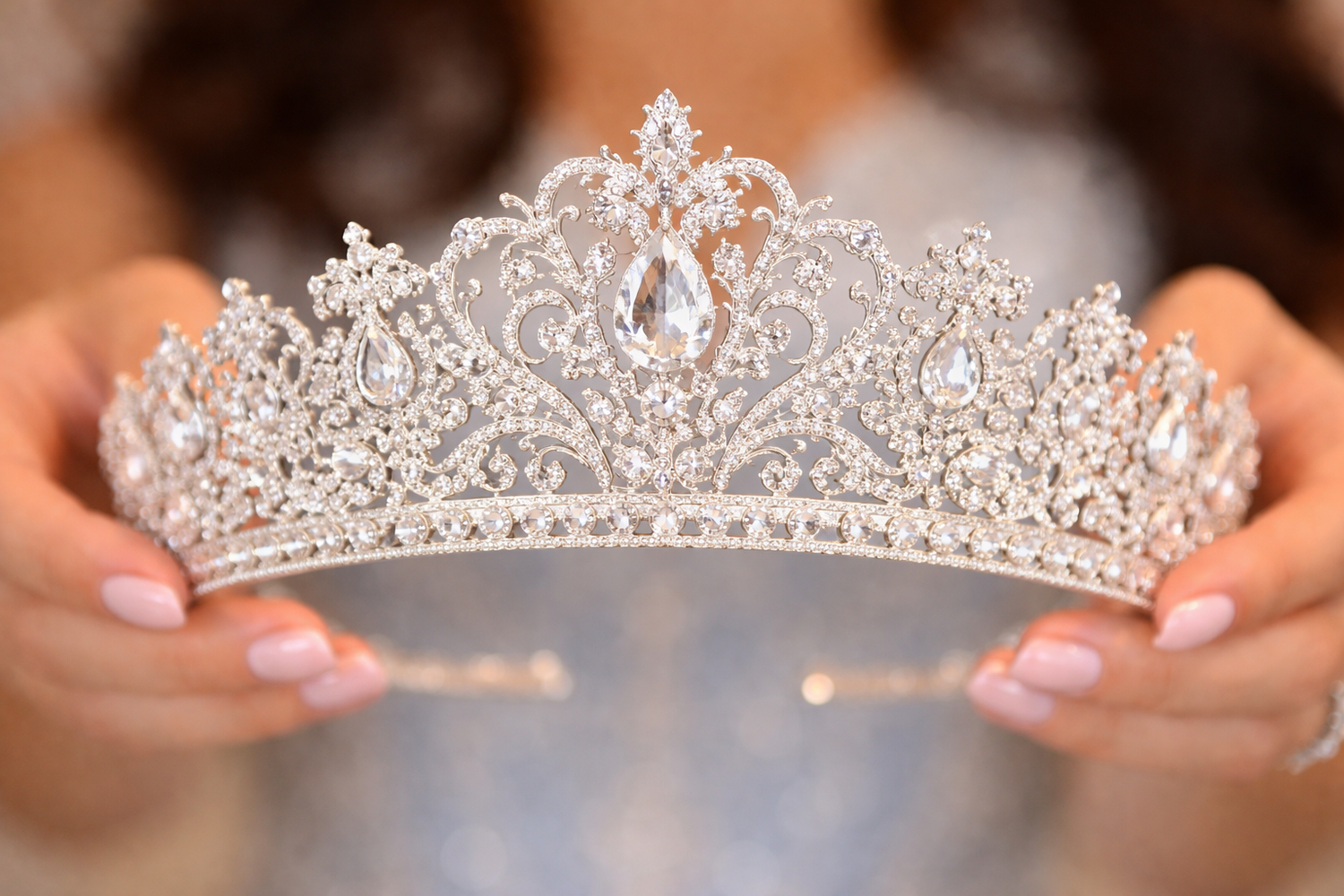 Una delicada tiara de quinceañera de plata y cristal, con intrincados patrones florales y piedras brillantes, sostenida sobre un fondo desen