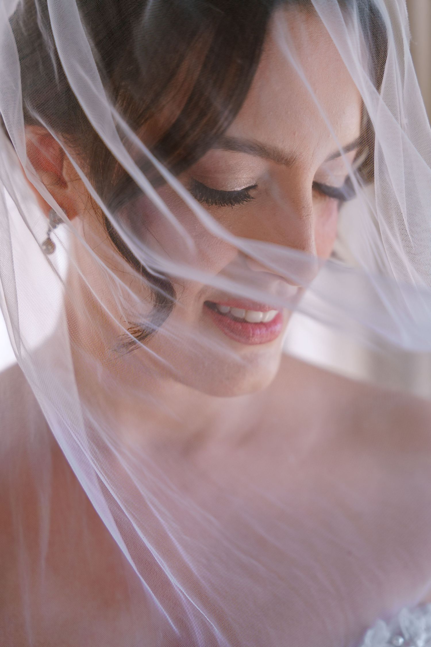 Una novia con un delicado velo blanco sonríe suavemente en un retrato nupcial etéreo en su boda.