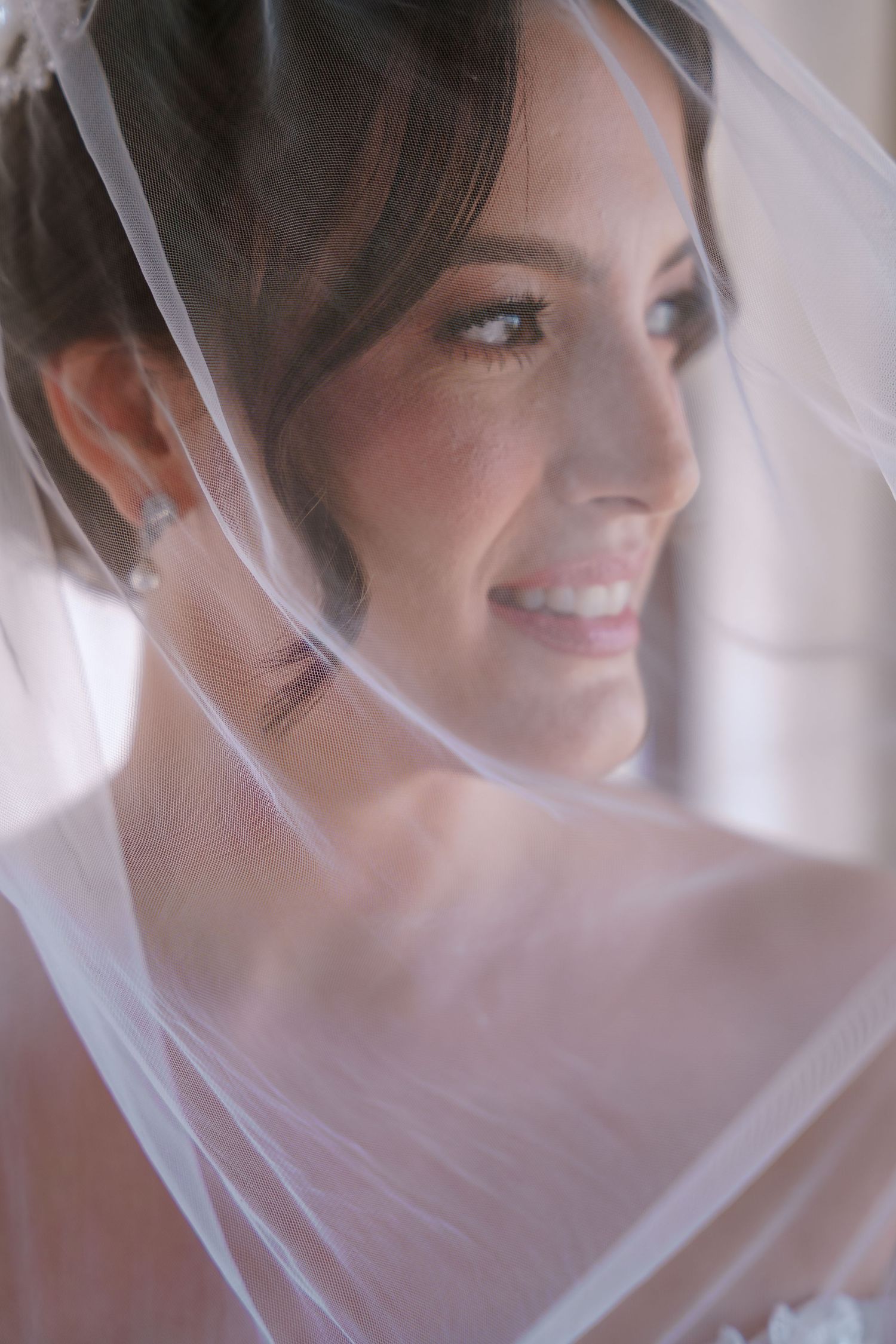 Una novia sonríe suavemente a través de un delicado velo blanco en un retrato nupcial romántico en su boda.