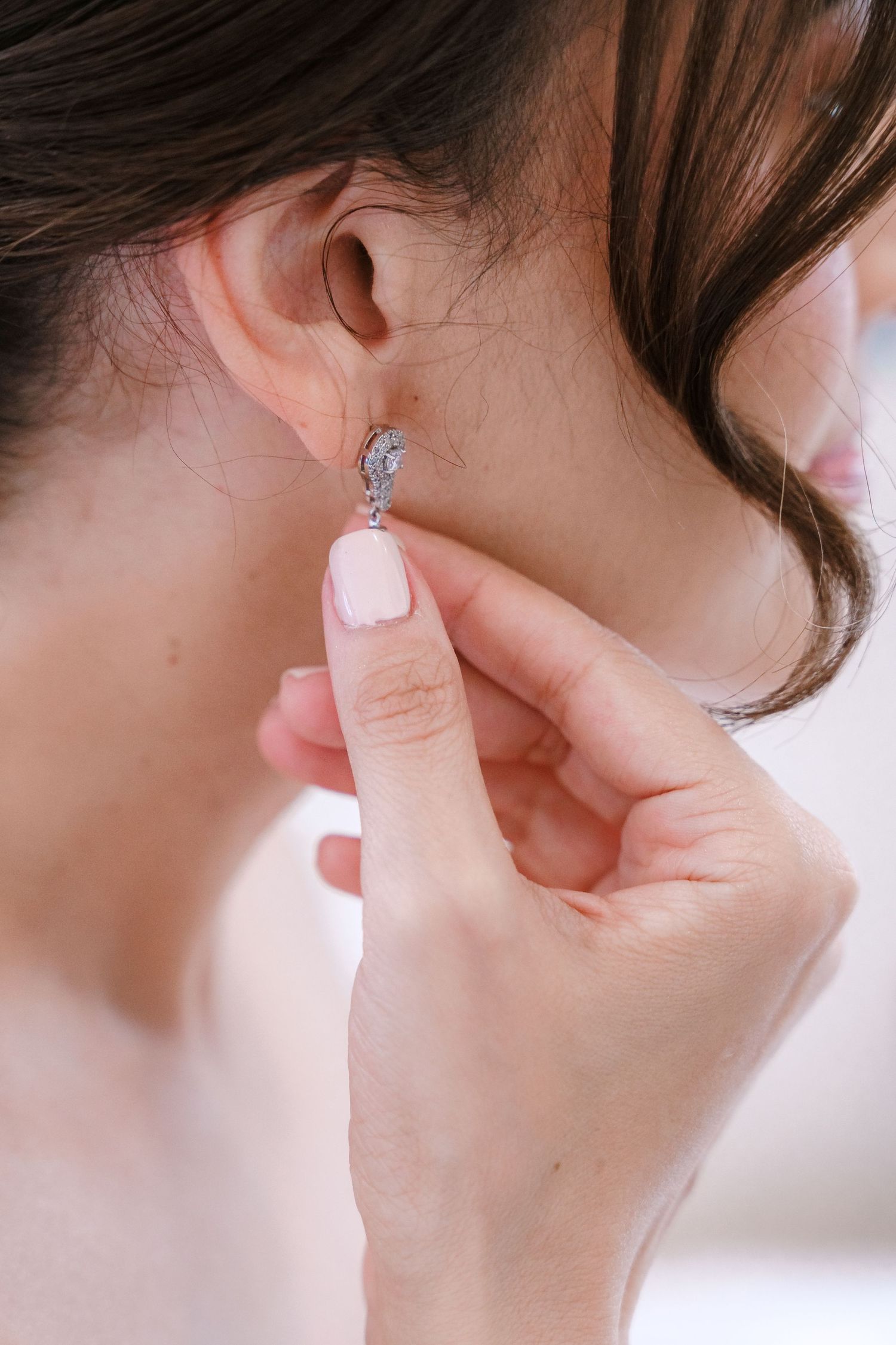 Serie de primeros planos que muestra cómo se colocan delicados aretes de plata en una oreja, con un fondo suave y desenfocado en su boda.