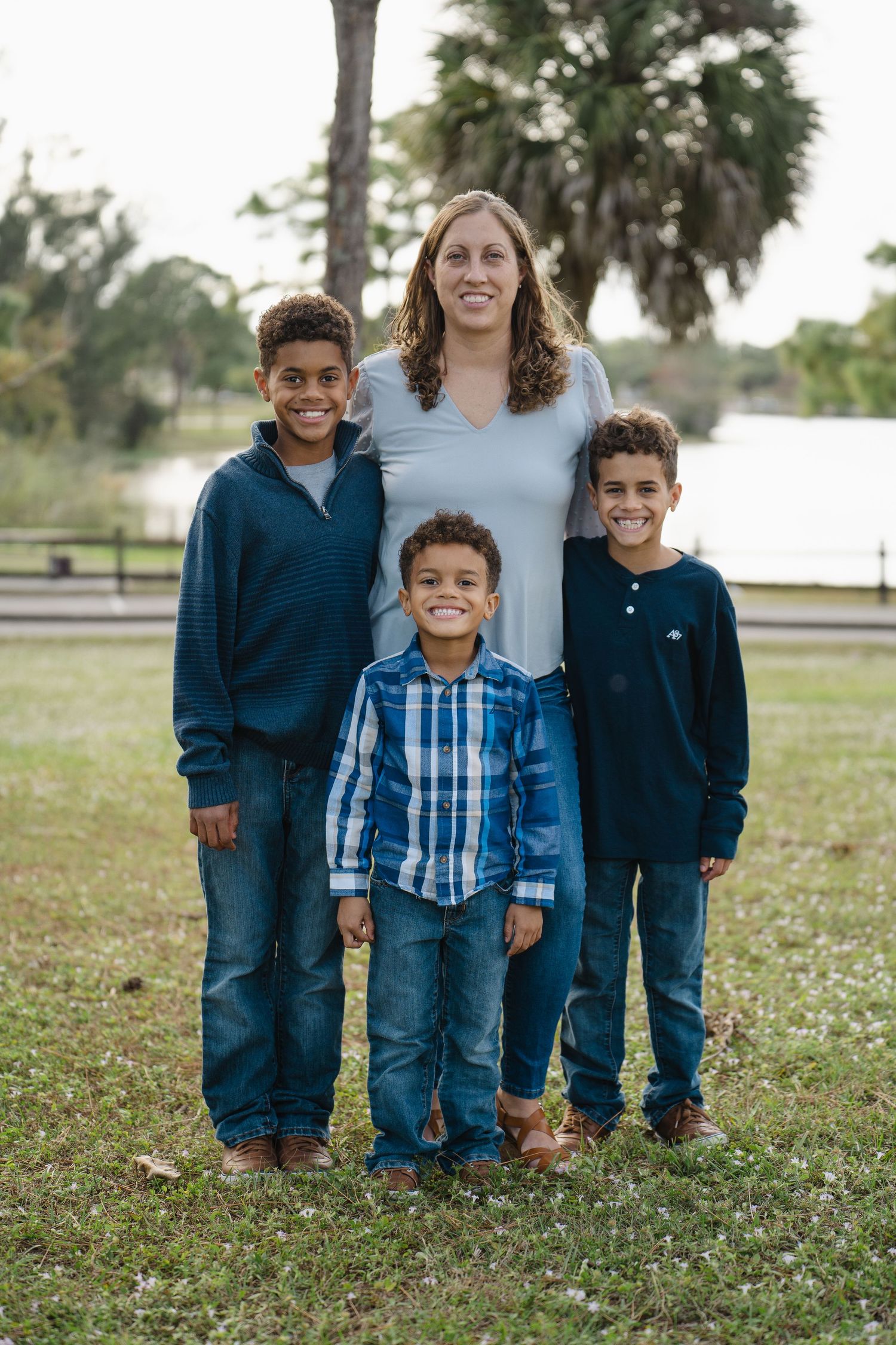 Family of four posing for a portrait at a park with palm trees and water in the background.