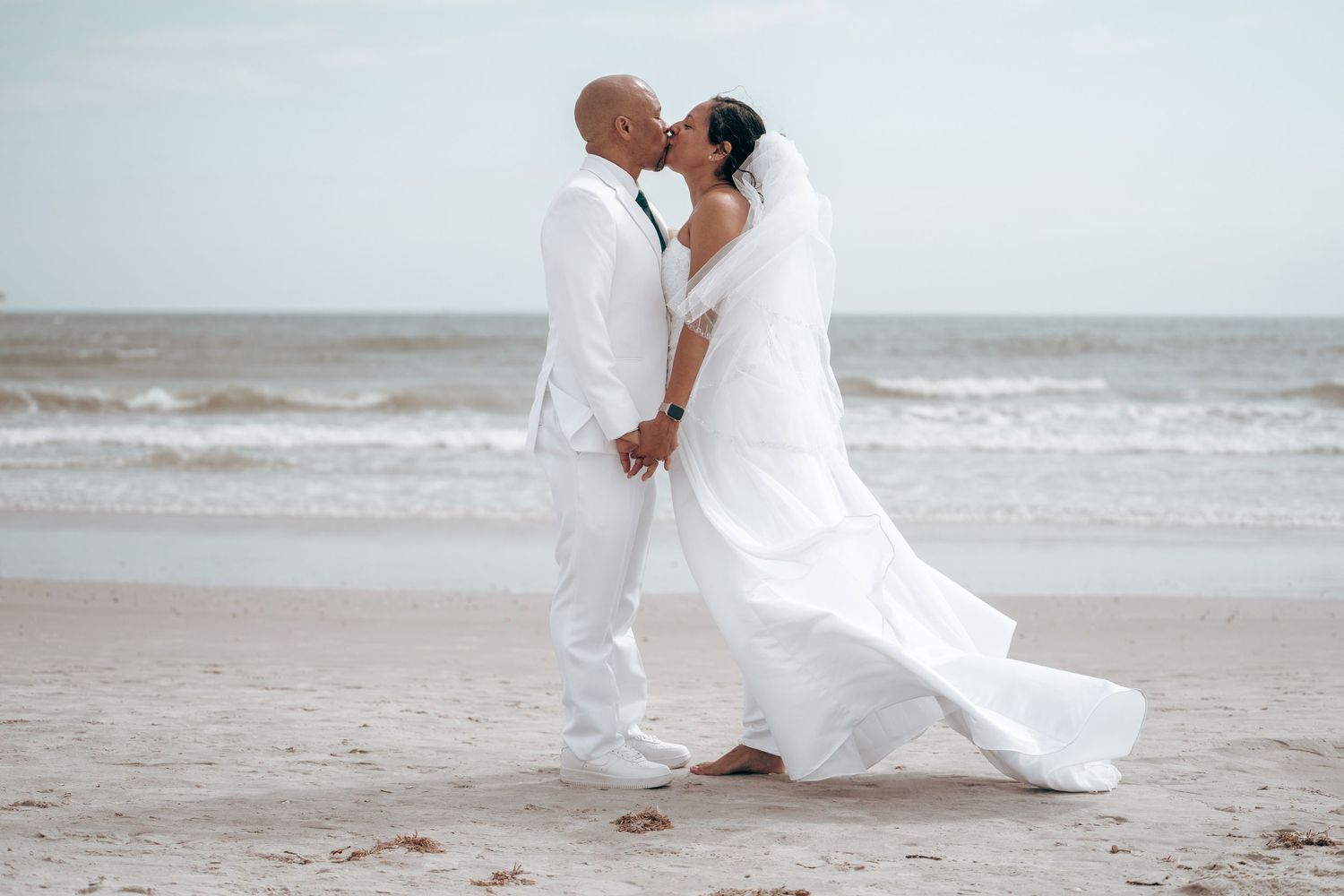 Intimate beach wedding portrait with couple in white embracing by the ocean.