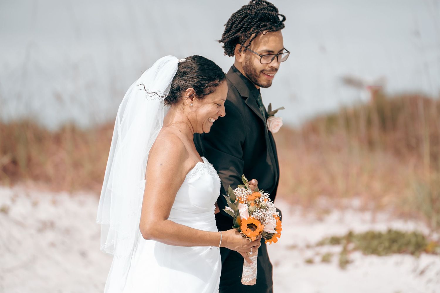 A joyful beach wedding moment captured with the bride holding an orange bouquet.