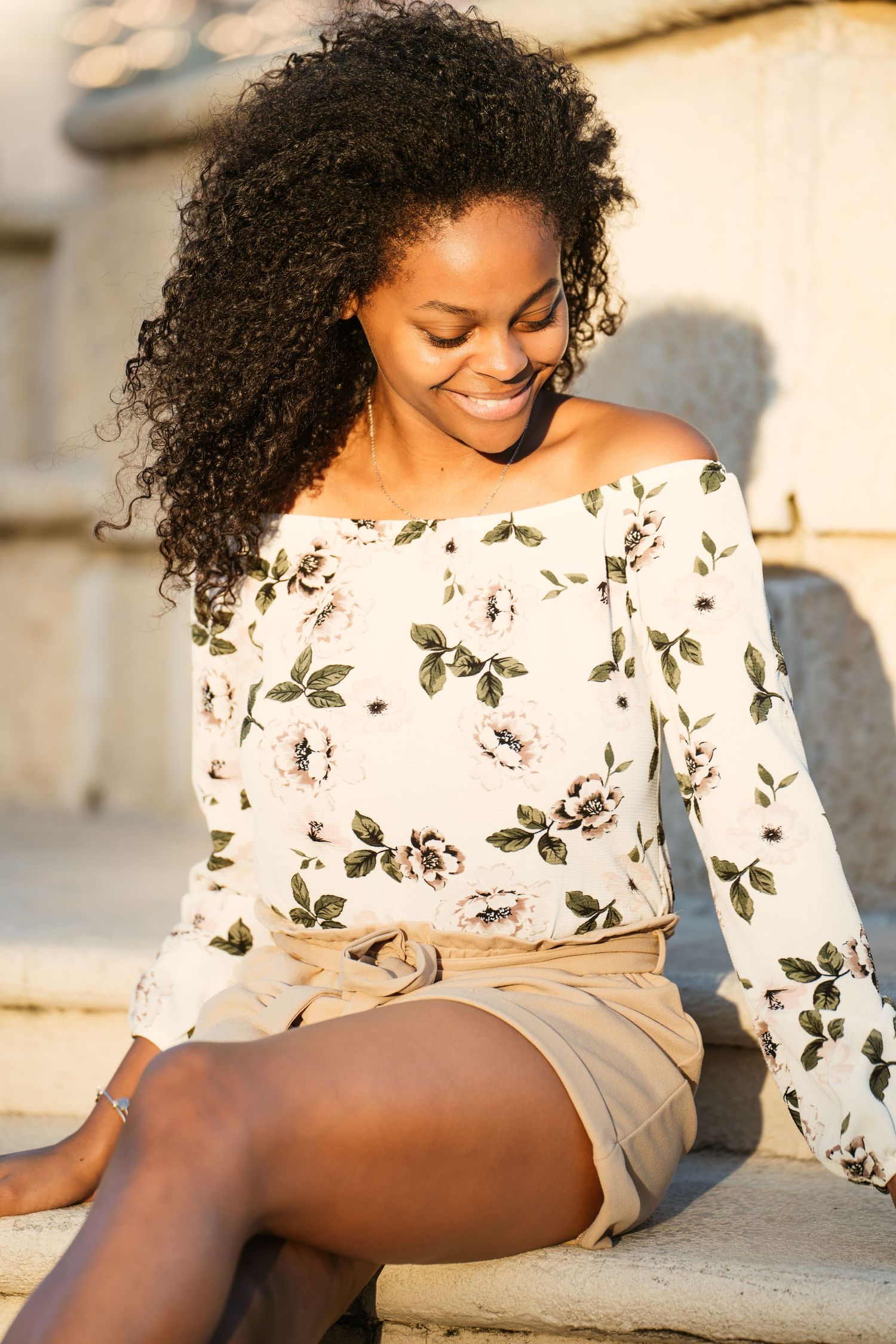 Off-shoulder floral print blouse paired with beige shorts in warm sunset lighting.