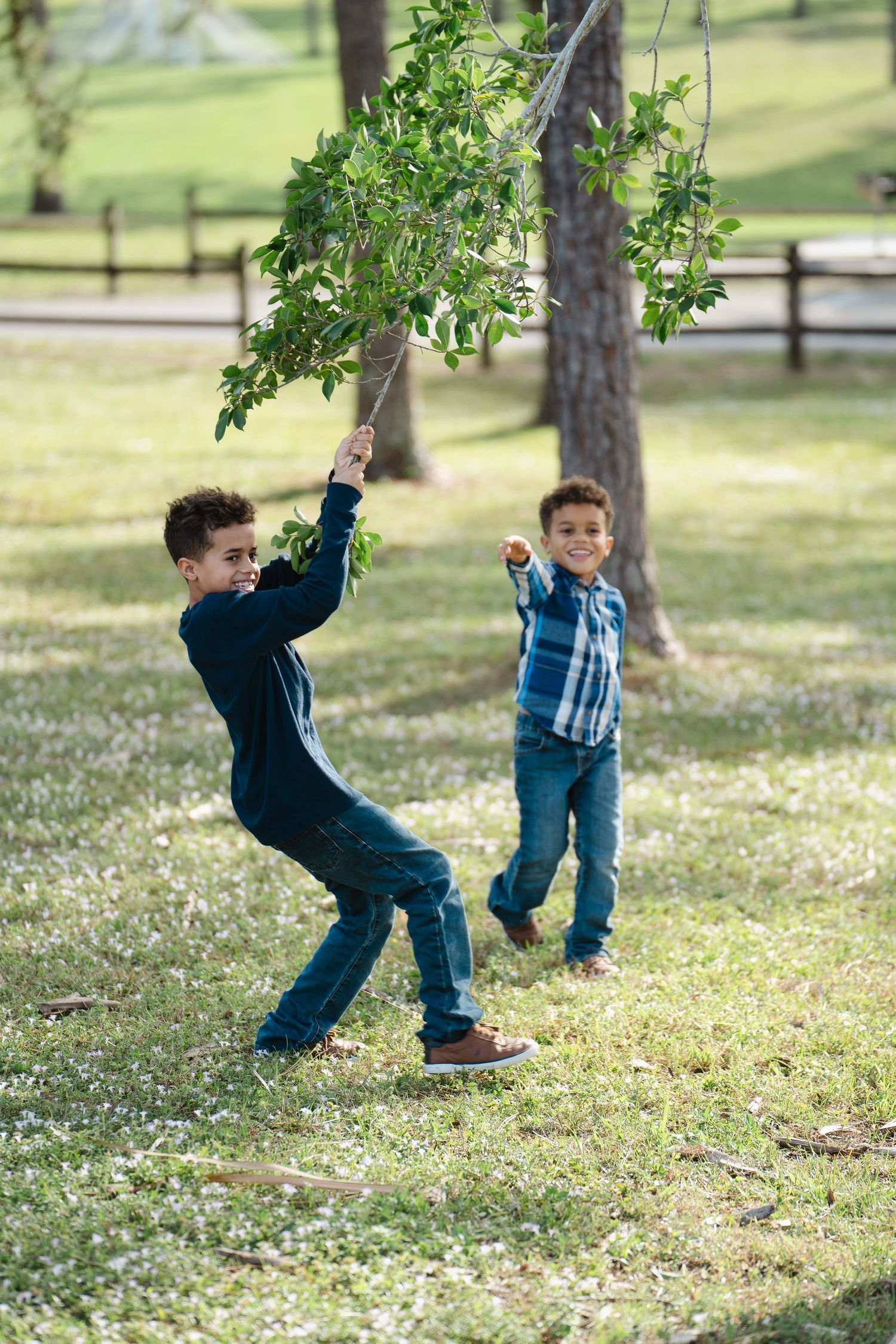 Two children playing with tree branches in a park on a sunny day.