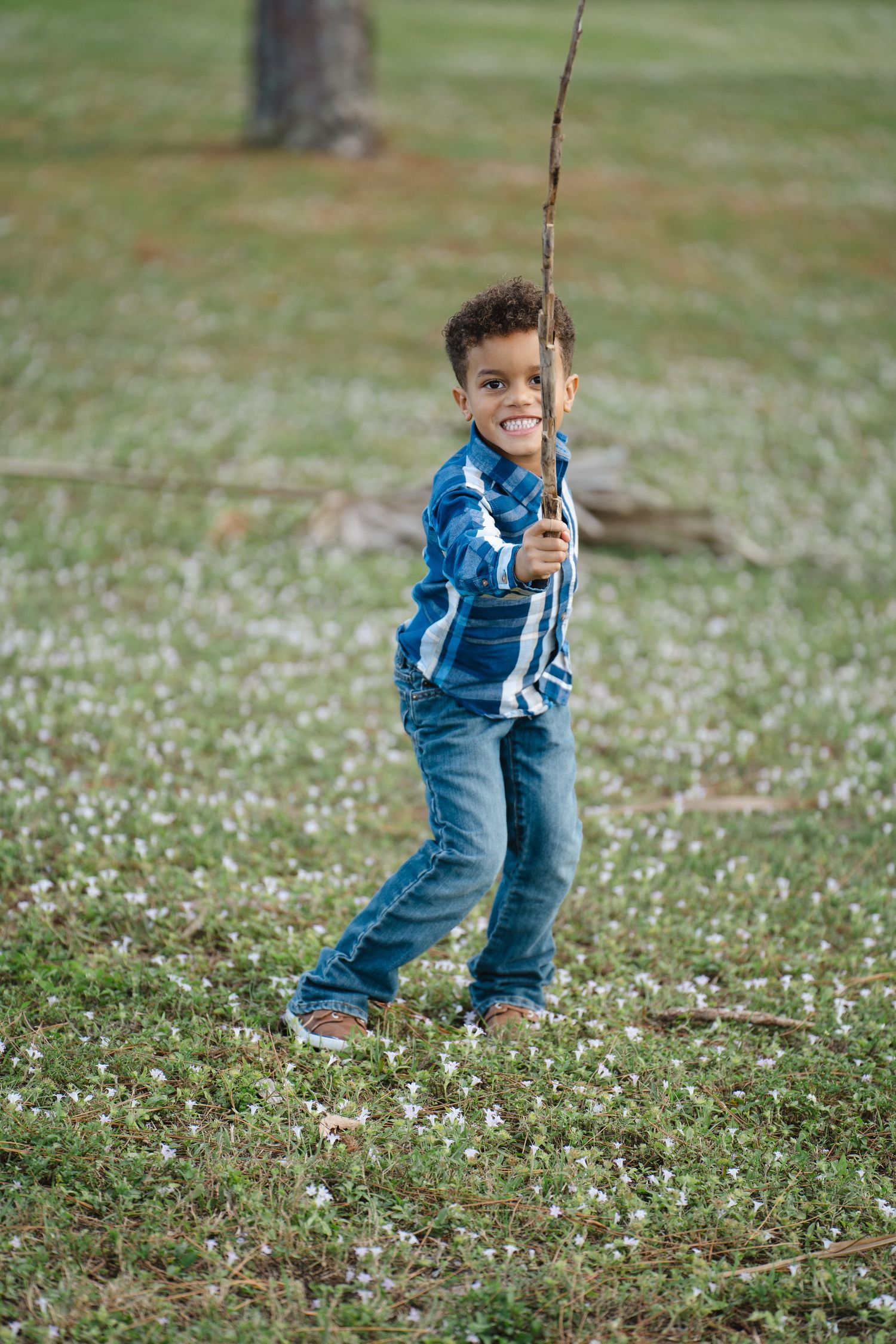 Young boy in blue plaid shirt holding fishing rod in flowering meadow.