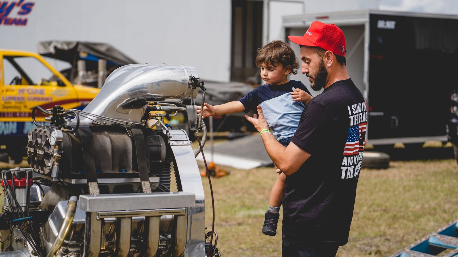 Two people working on mechanical equipment at an outdoor motorsport event.