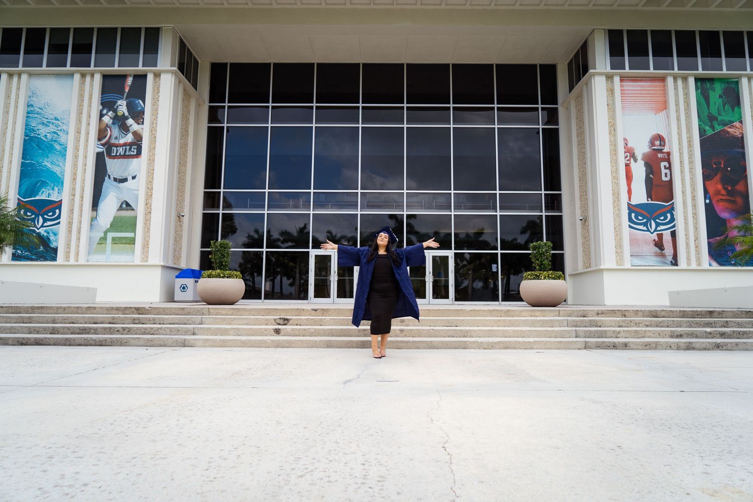 Graduate in blue regalia walking towards modern university building entrance.