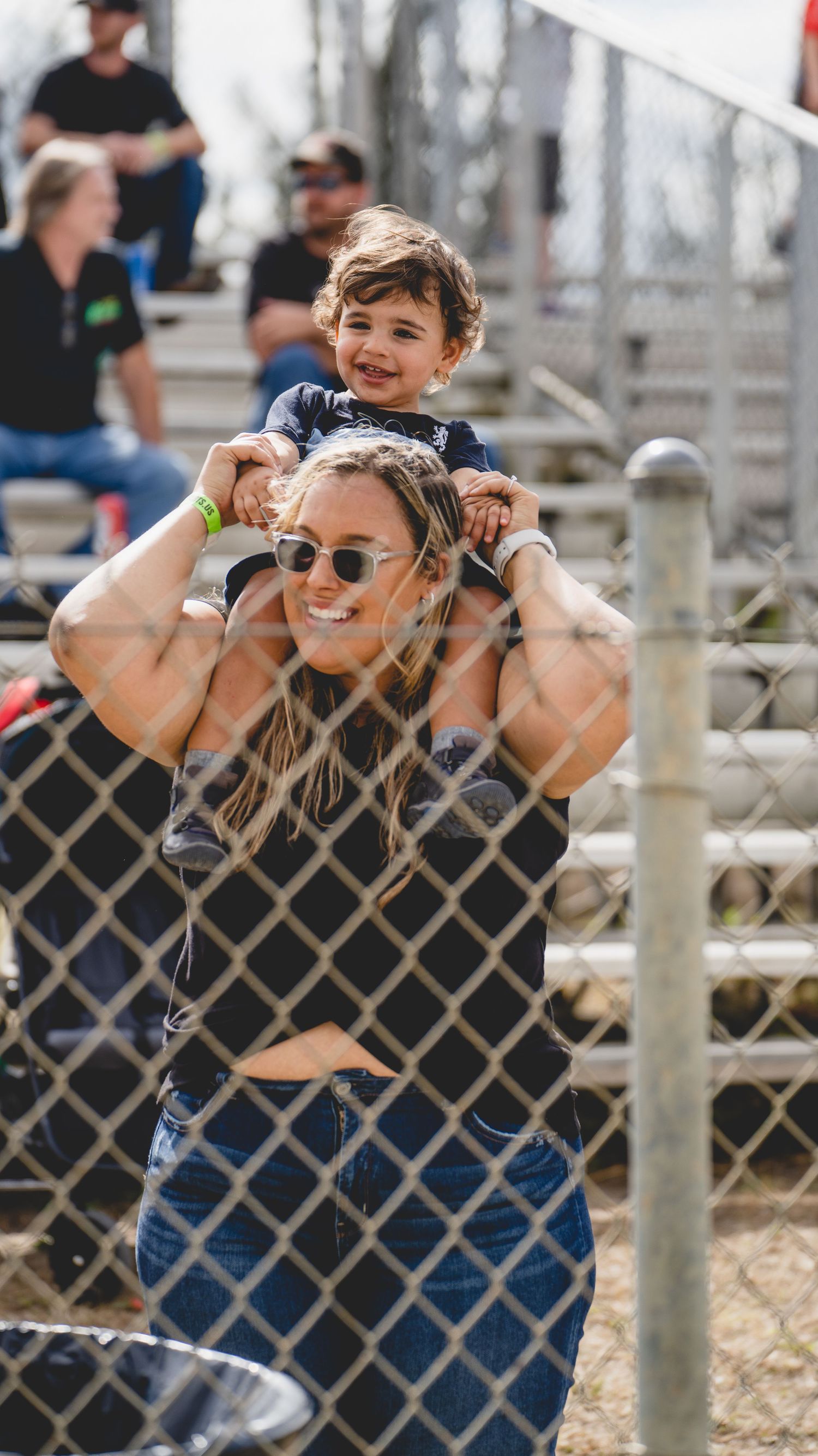 Parent and child share a joyful moment by a chain link fence at an outdoor event.