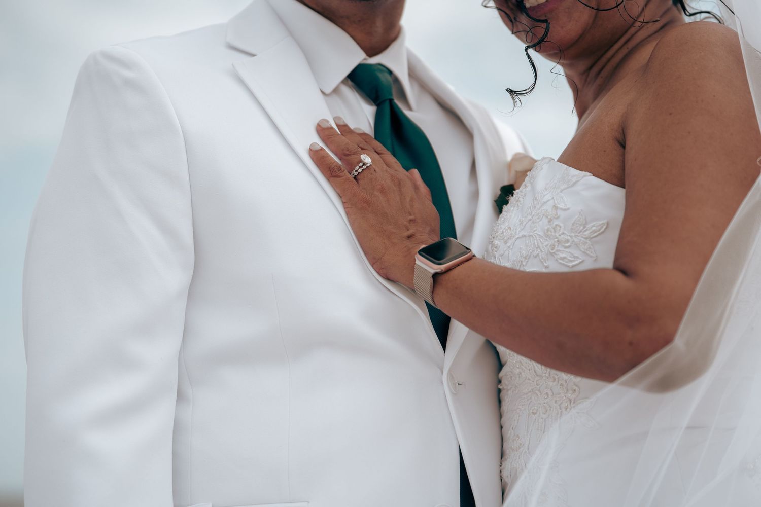 Close up of a couple's wedding attire showing white suit jacket and engagement ring.