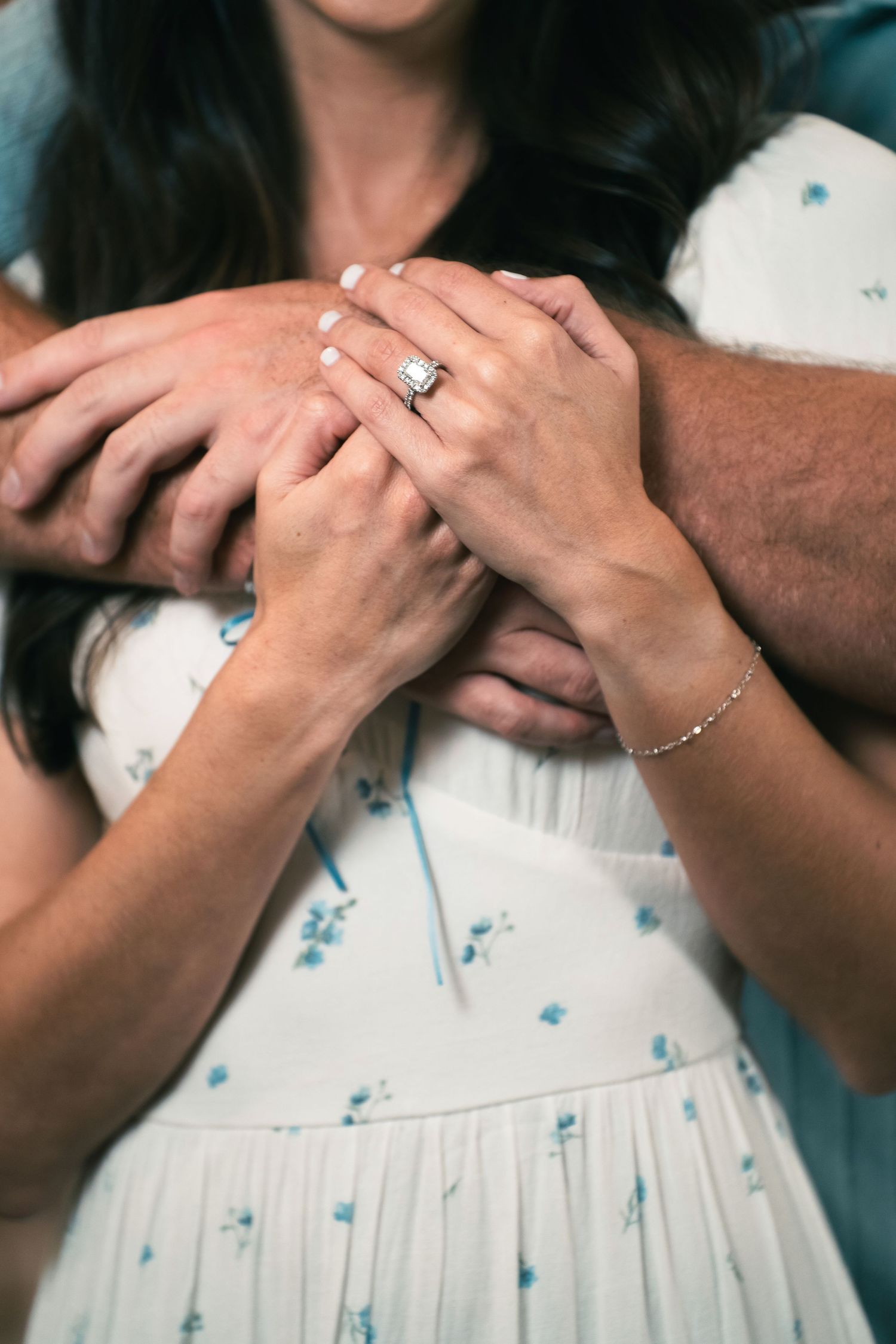 Close up of hands showing off an engagement ring on a floral dress.