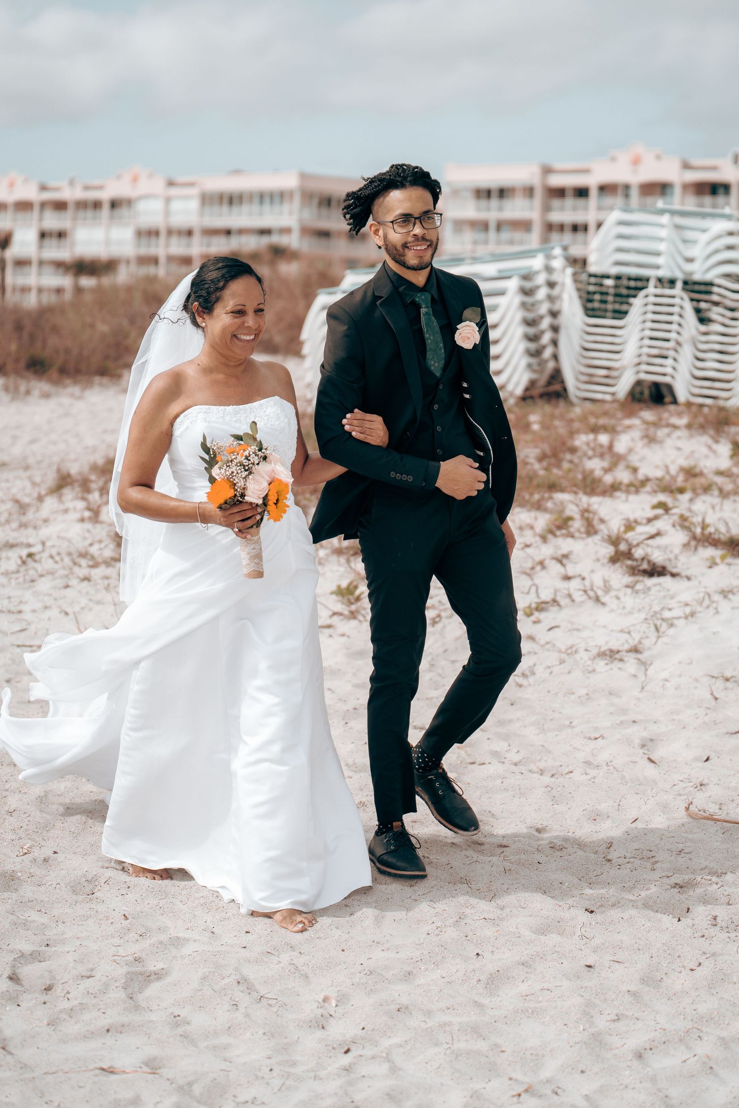 Newlywed couple walking arm in arm on beach with white wedding attire.