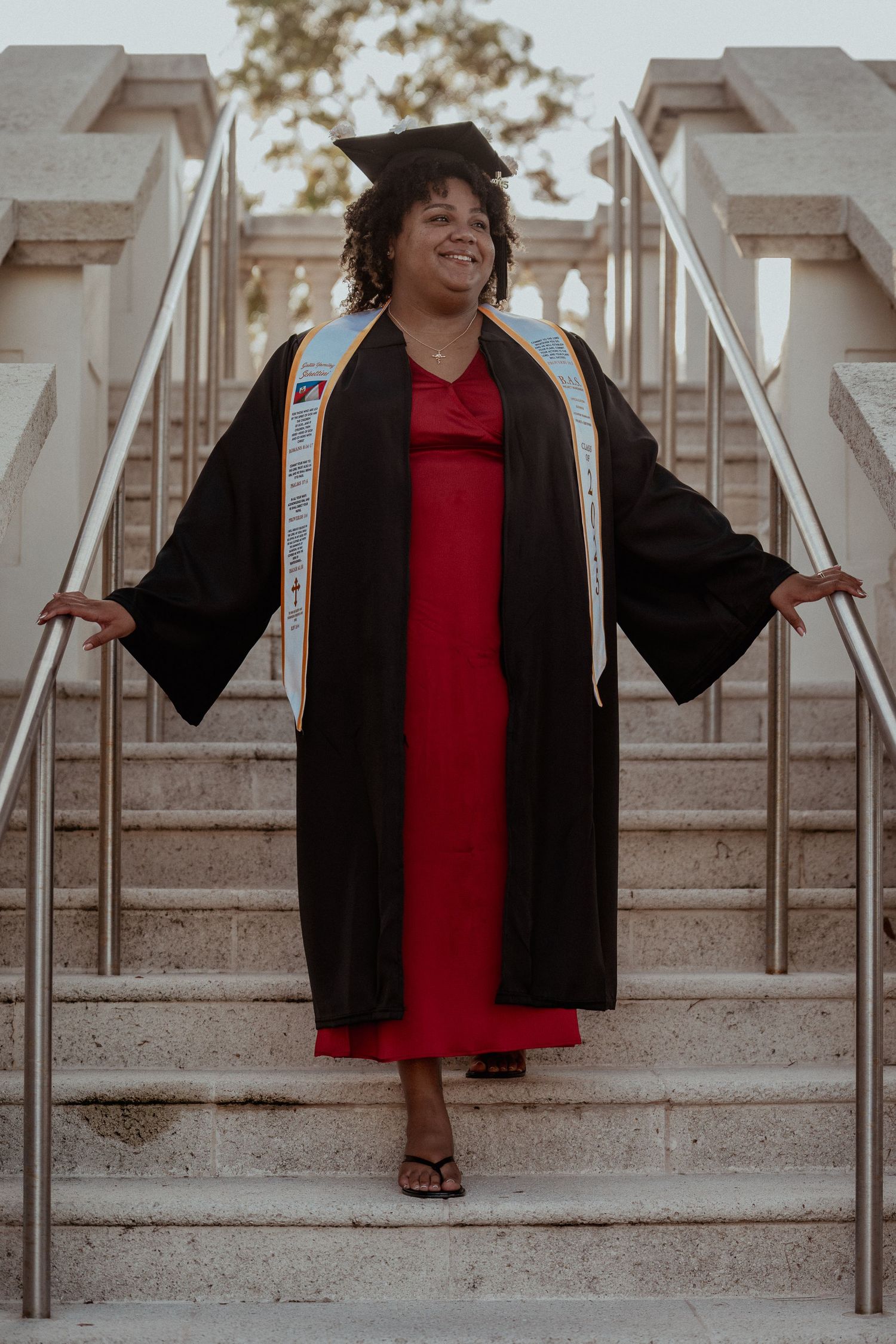 A graduate in a black gown and red dress poses joyfully on concrete steps in a celebratory photo series.