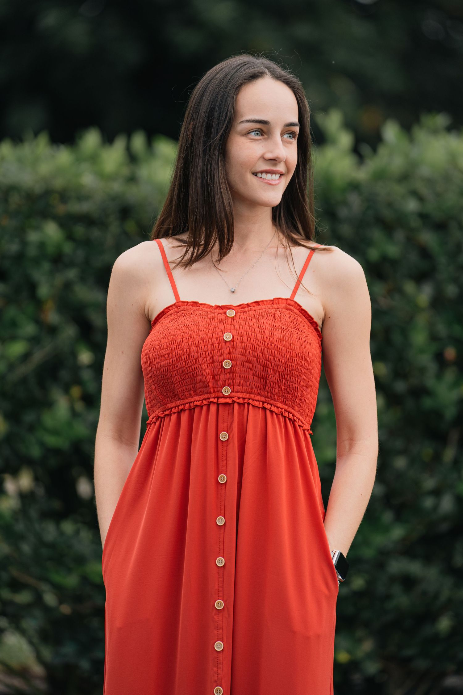Red button-down sundress styled against lush green garden backdrop.
