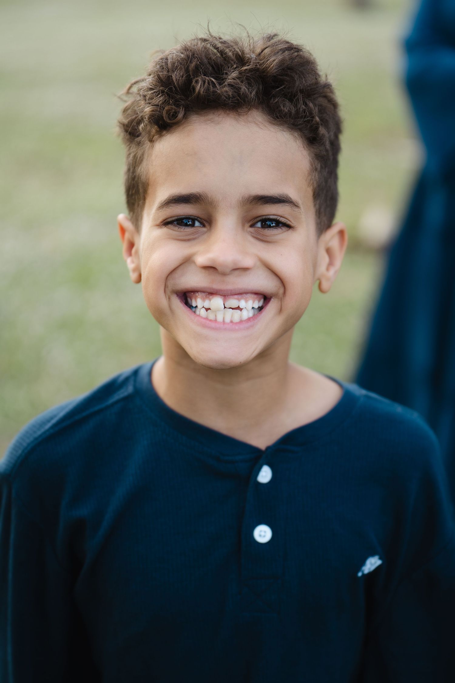 Young boy in navy henley shirt smiling brightly at camera.