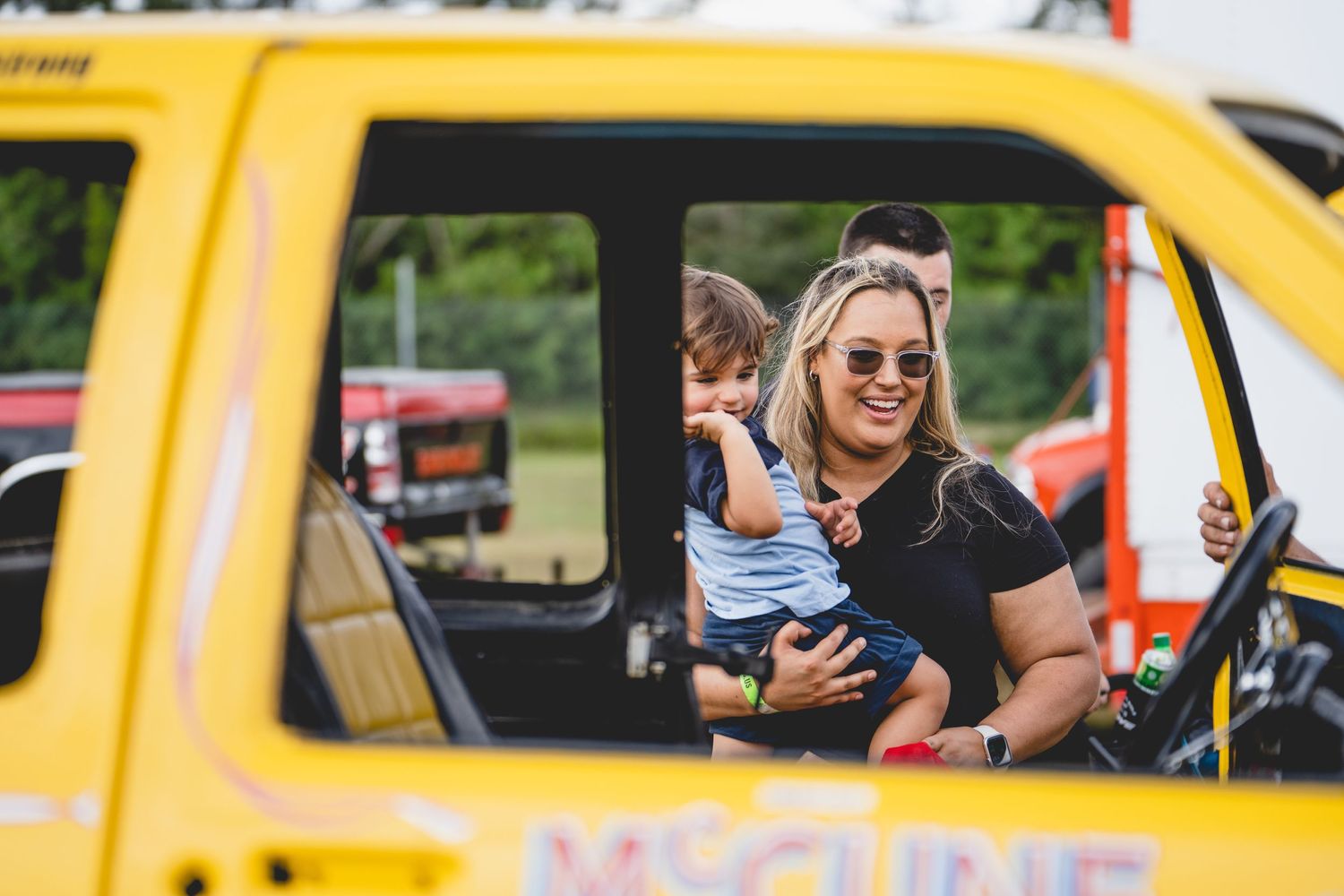 Person with child in yellow vehicle smiling through window.