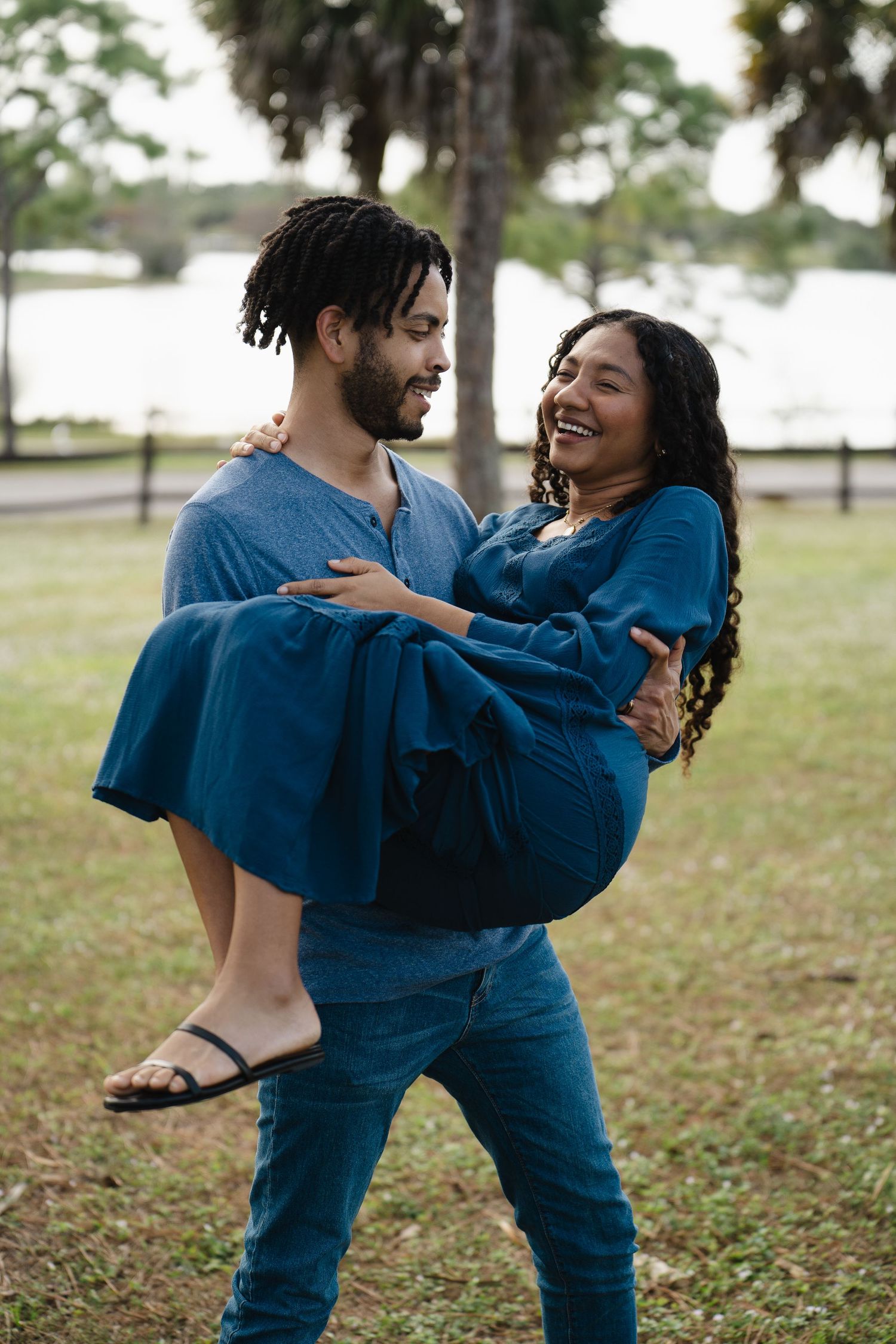 Joyful couple in matching blue outfits playing and laughing in park.