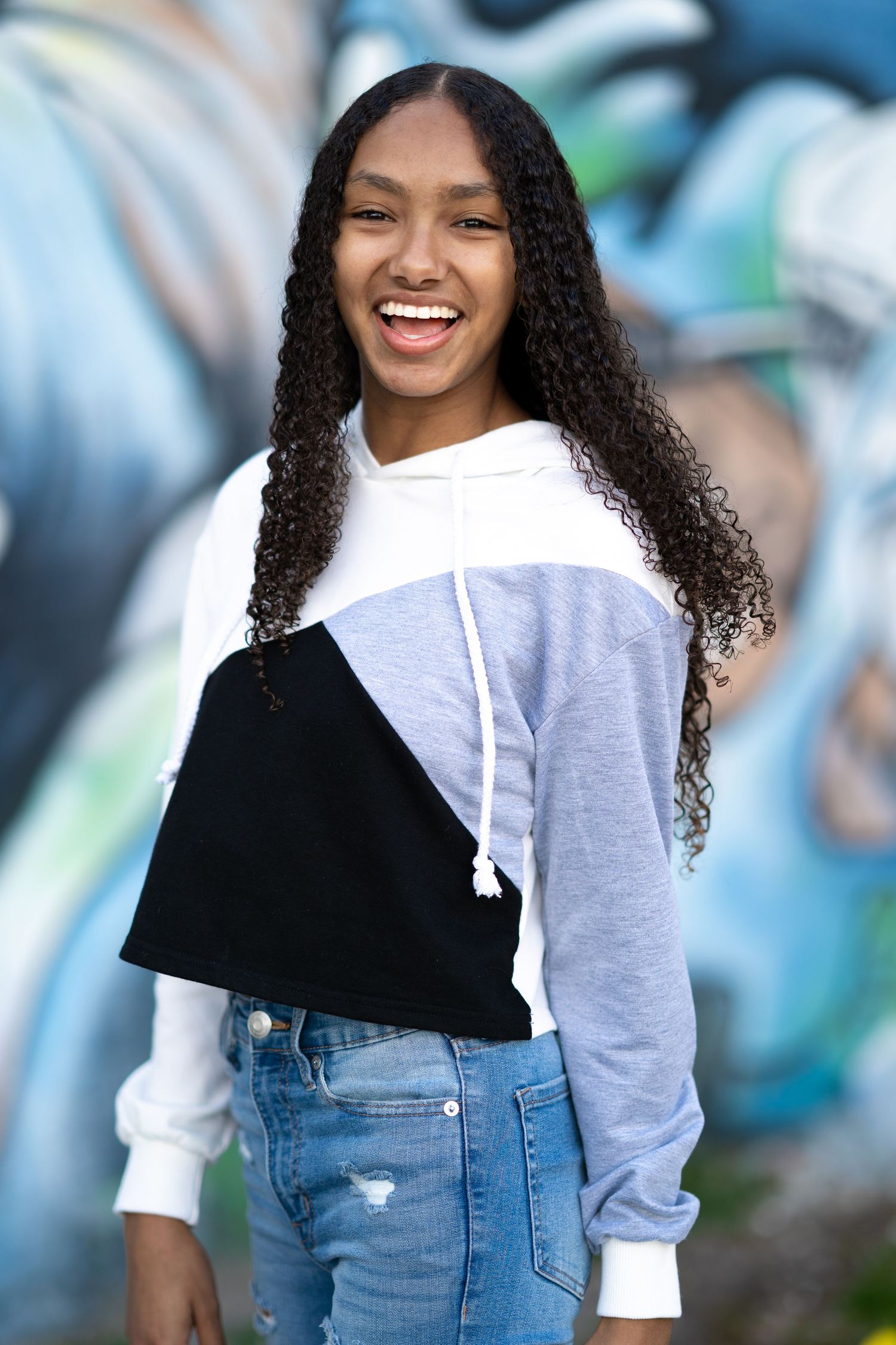 Color block hoodie and distressed jeans outfit against vibrant graffiti wall.