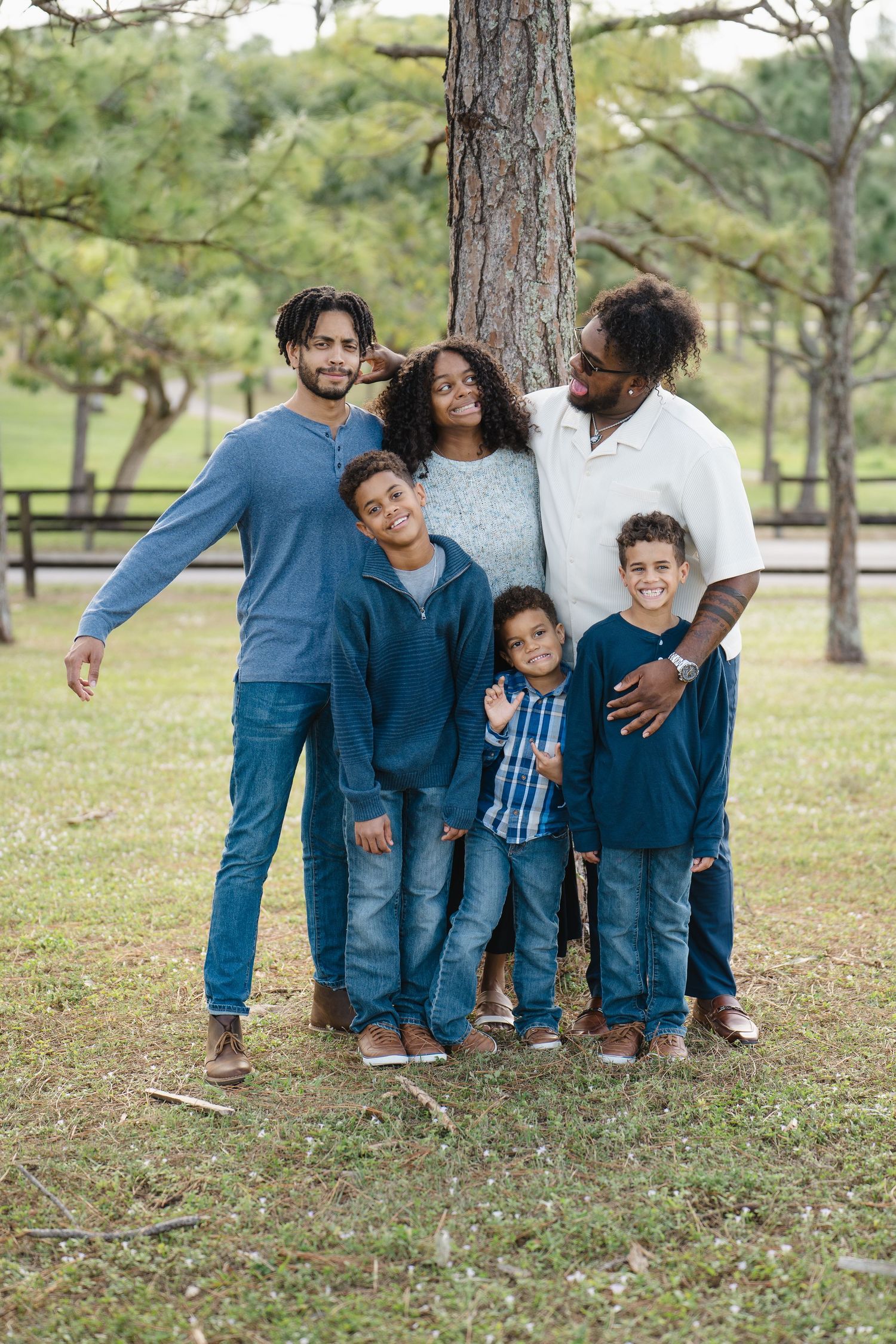 Happy family of six posing together outdoors under pine trees.