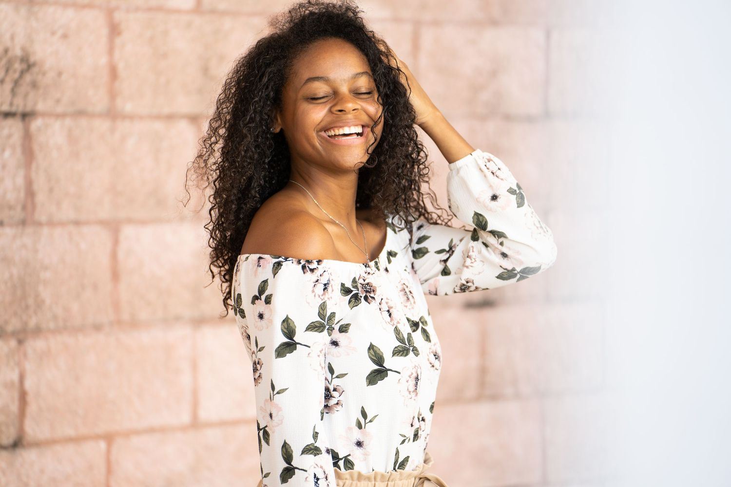 Fashionable off-shoulder floral top with natural curly hair against a textured wall in natural lighting.