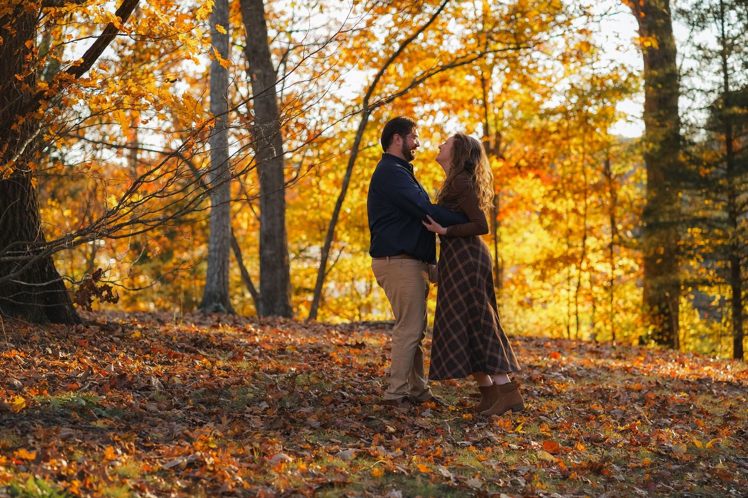 Couple holding hands in an autumn forest with vibrant orange and yellow foliage during a fall engagement photo session.