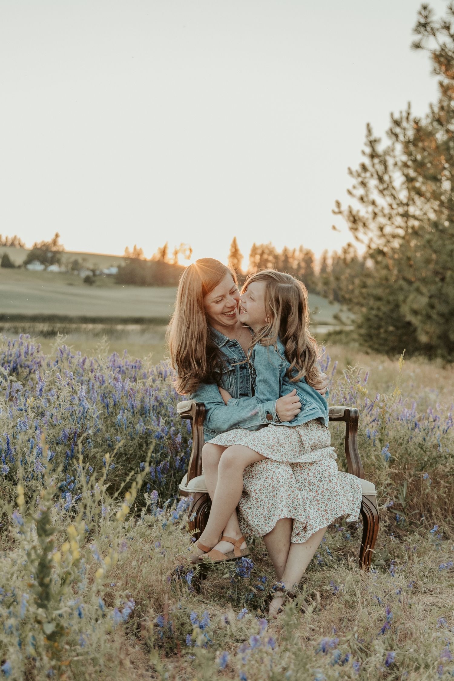 mom daughter dressed in matching jean jacket and floral dress sitting in purple flower field at sunset with spokane phot