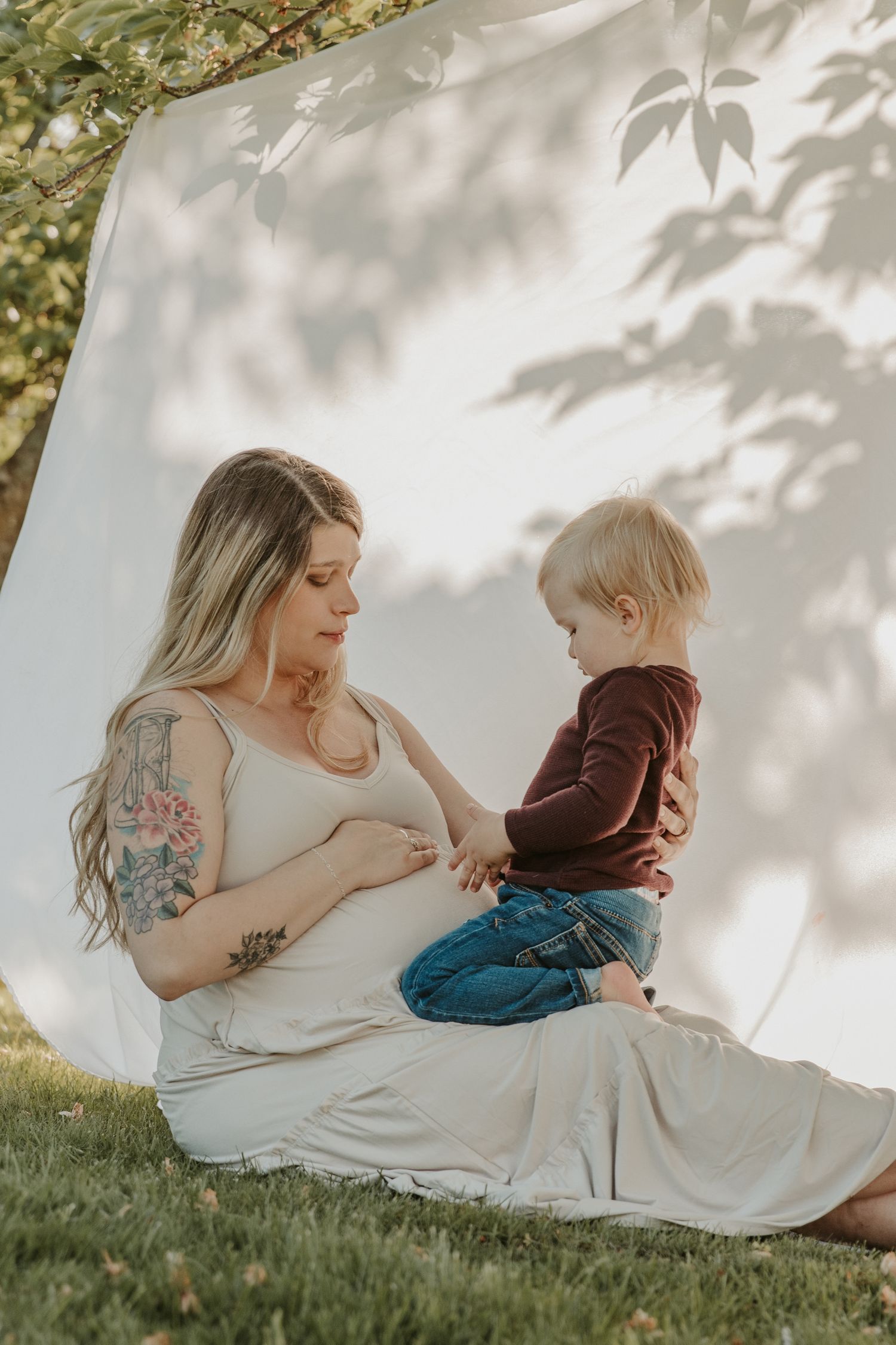 pregnant mom and son in the grass with a white sheet background with spokane family photographer