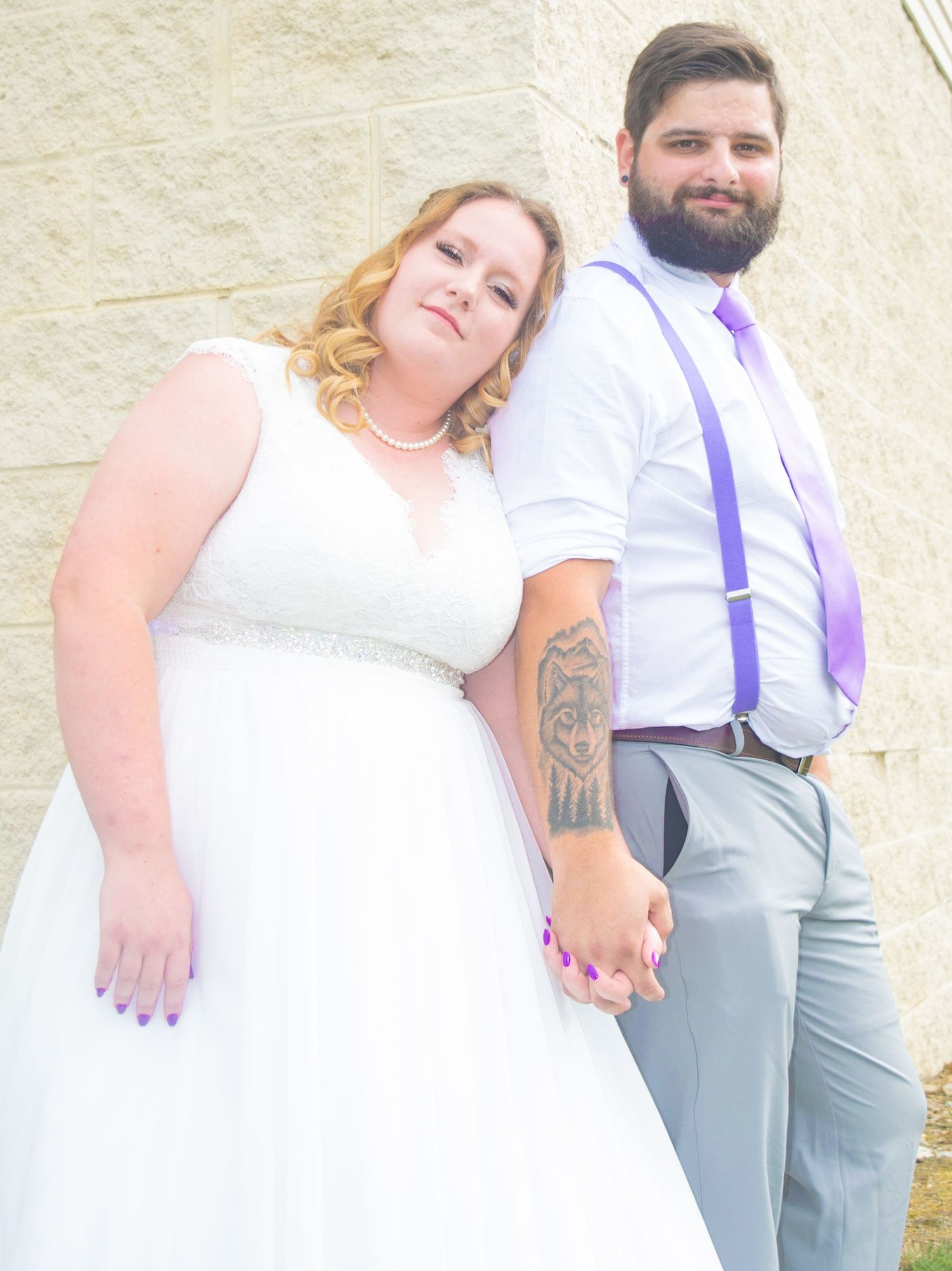 Wedding couple in white dress and grey suit with purple accents pose together outdoors.