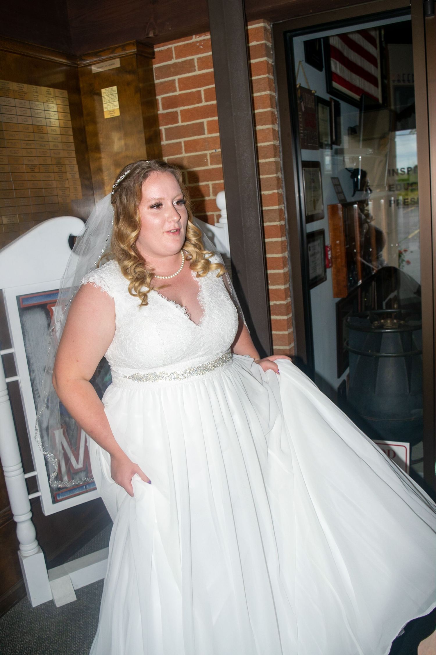 Bride in flowing white dress poses in front of brick storefront with classic styling.