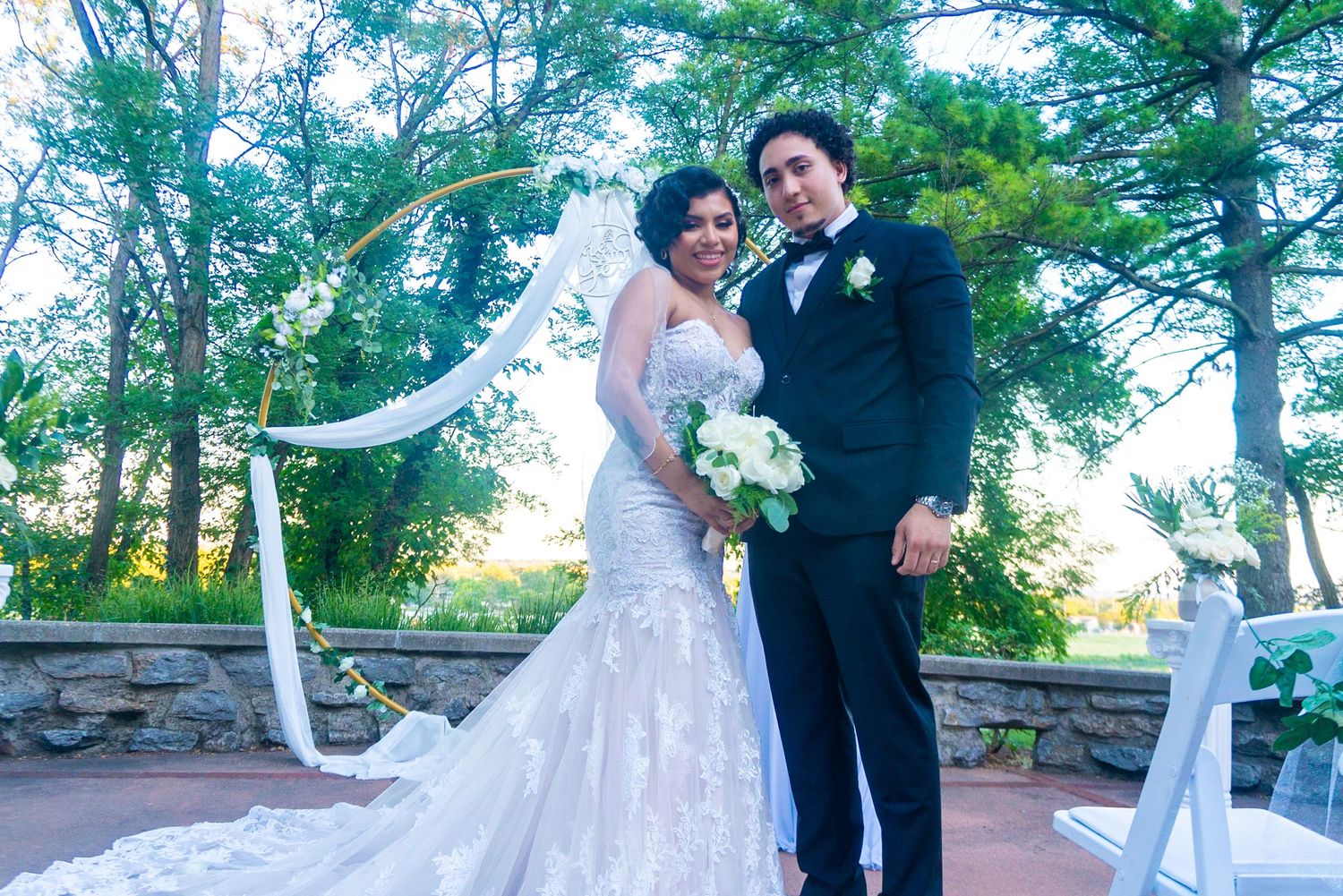 Wedding couple dances and celebrates on outdoor stone terrace surrounded by trees.