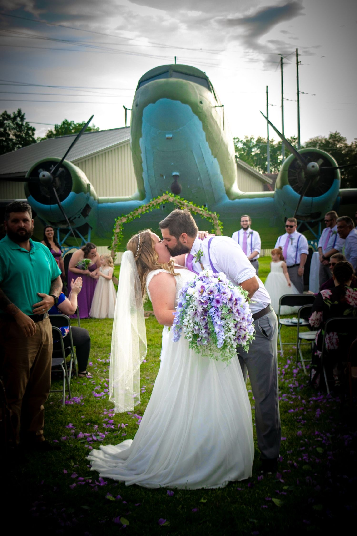 Wedding ceremony taking place in front of a vintage blue airplane with floral decorations.