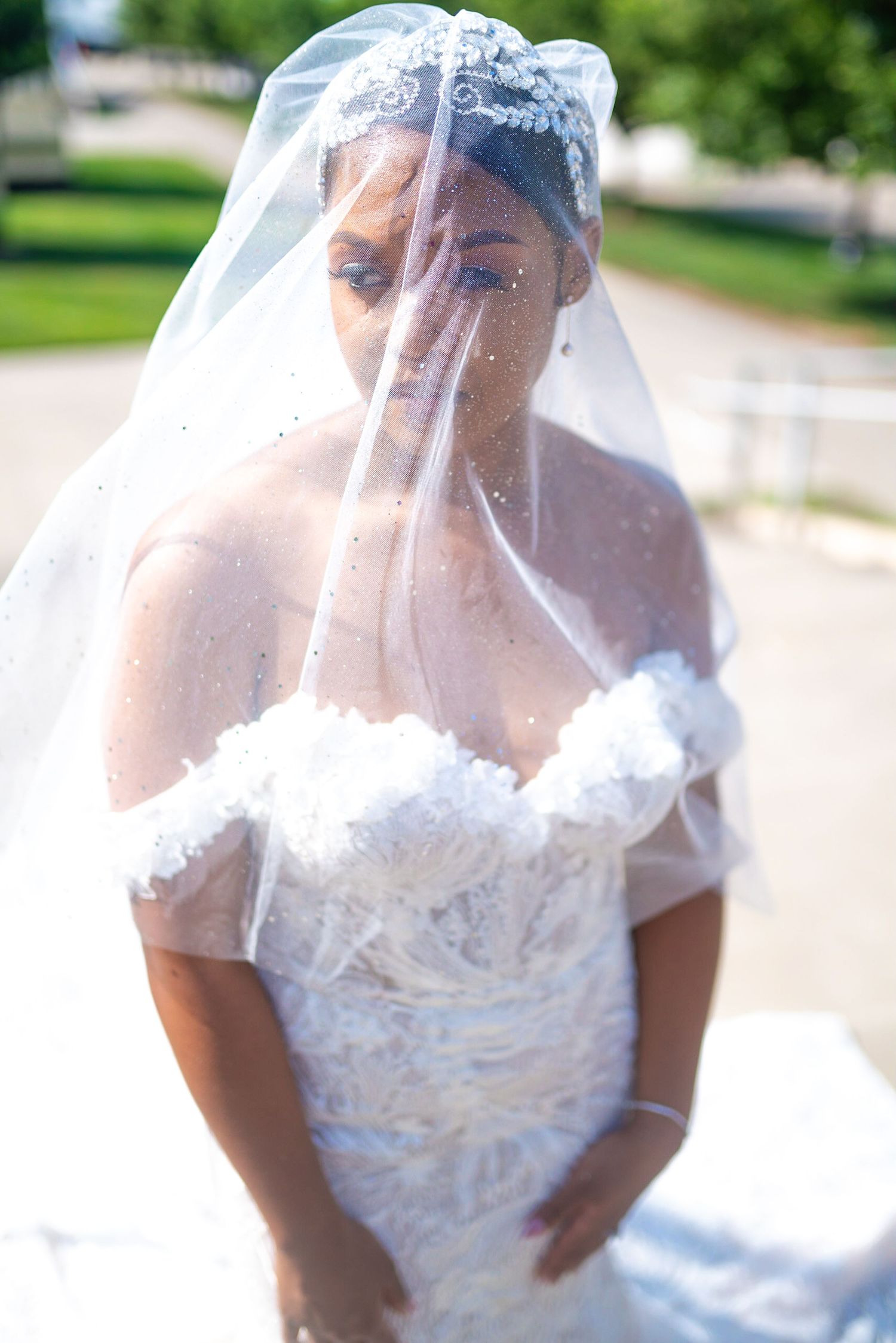 Close-up of bride wearing delicate lace veil and strapless wedding gown outdoors.