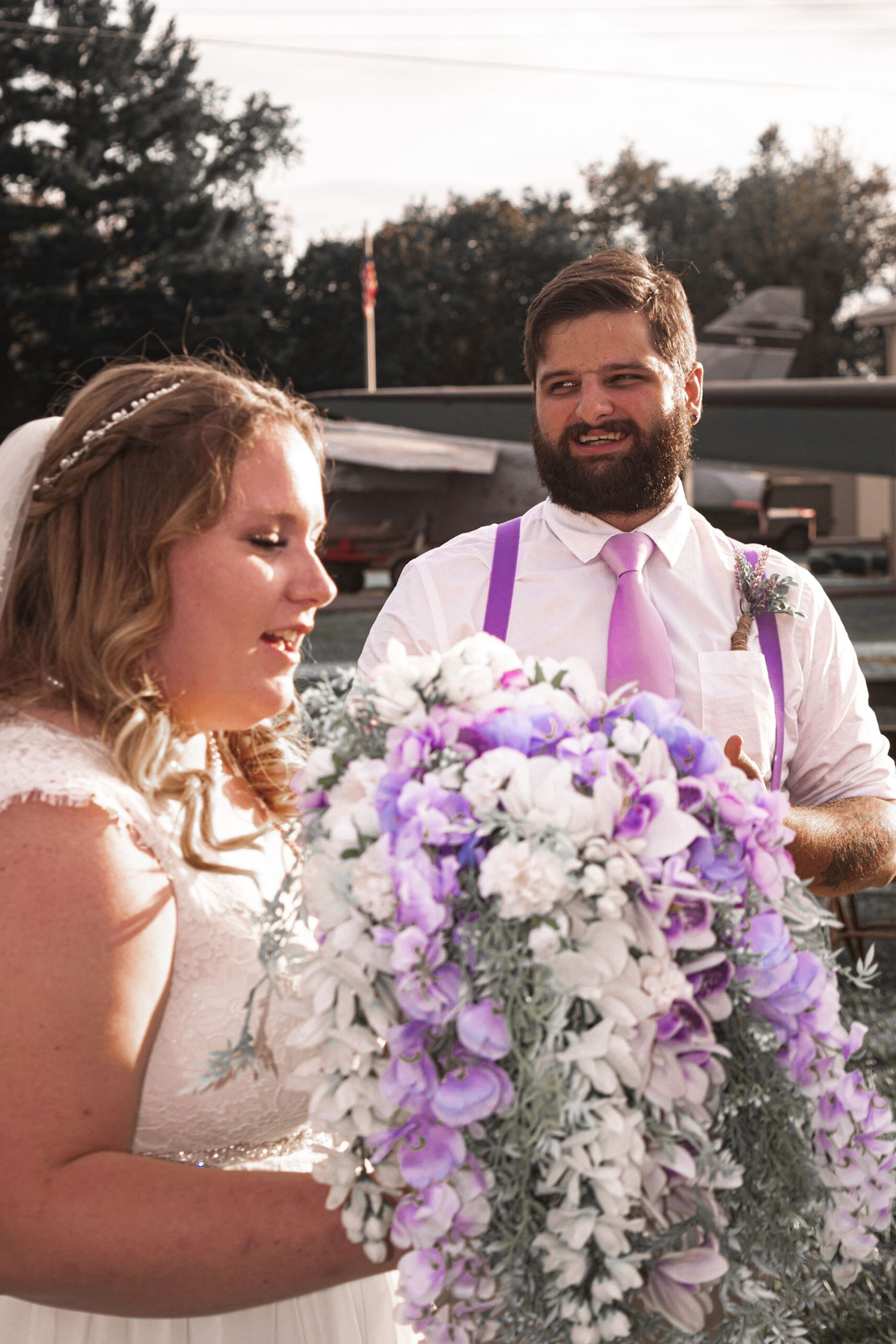 Wedding couple sharing intimate moment with purple and white floral bouquet at sunset.
