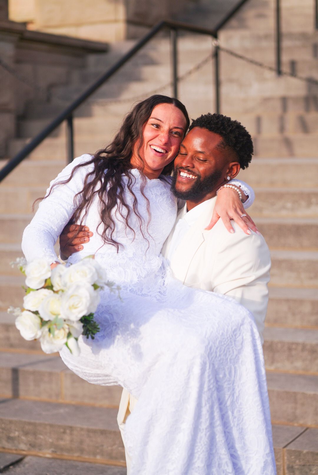 Joyful wedding couple embracing on stone steps during their photoshoot.