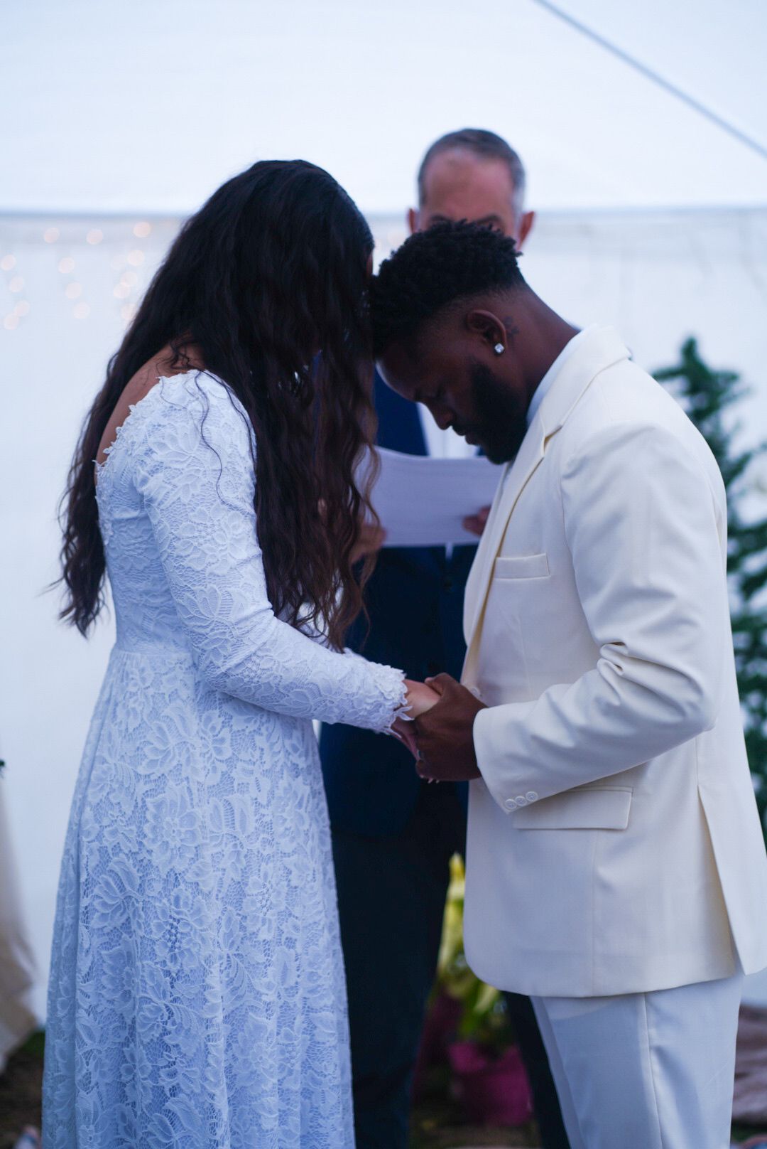 A couple in matching white outfits embracing during their wedding ceremony outdoors.