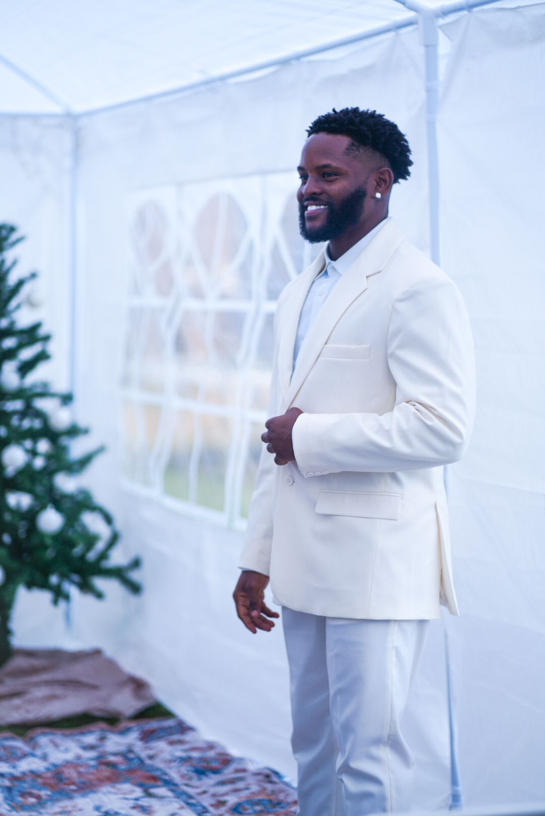 Person in white suit smiles during wedding celebration in tent setting.
