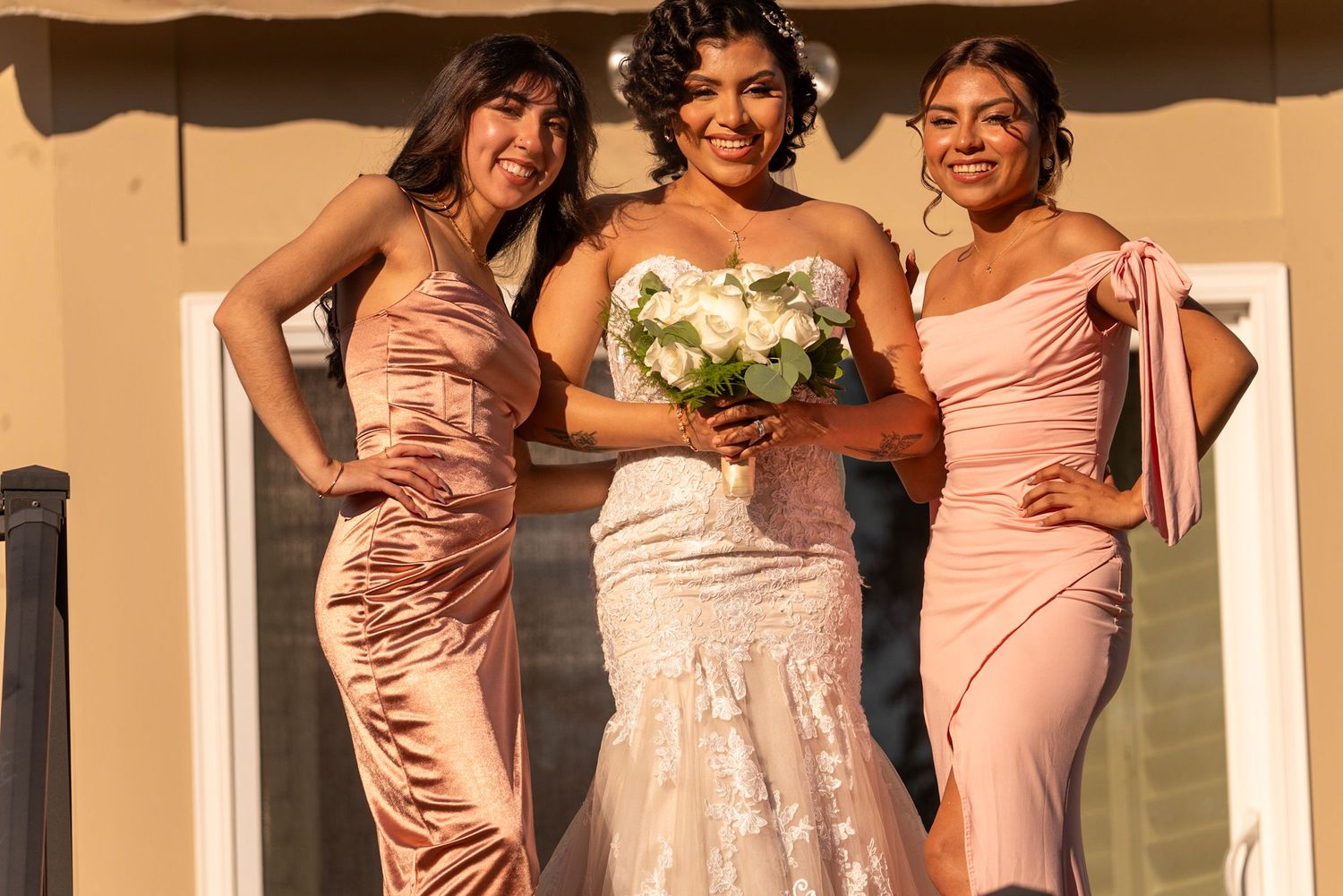 Bridesmaids in blush pink dresses pose together smiling at a wedding celebration.