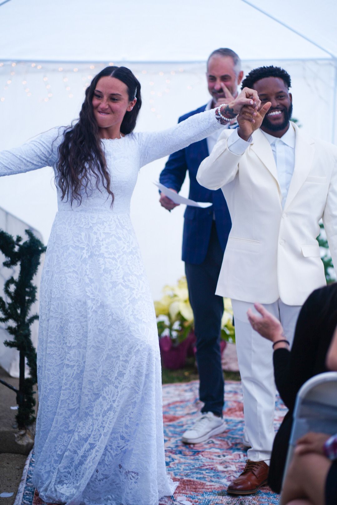 Wedding couple in white lace dress and suit dancing joyfully at their outdoor celebration.