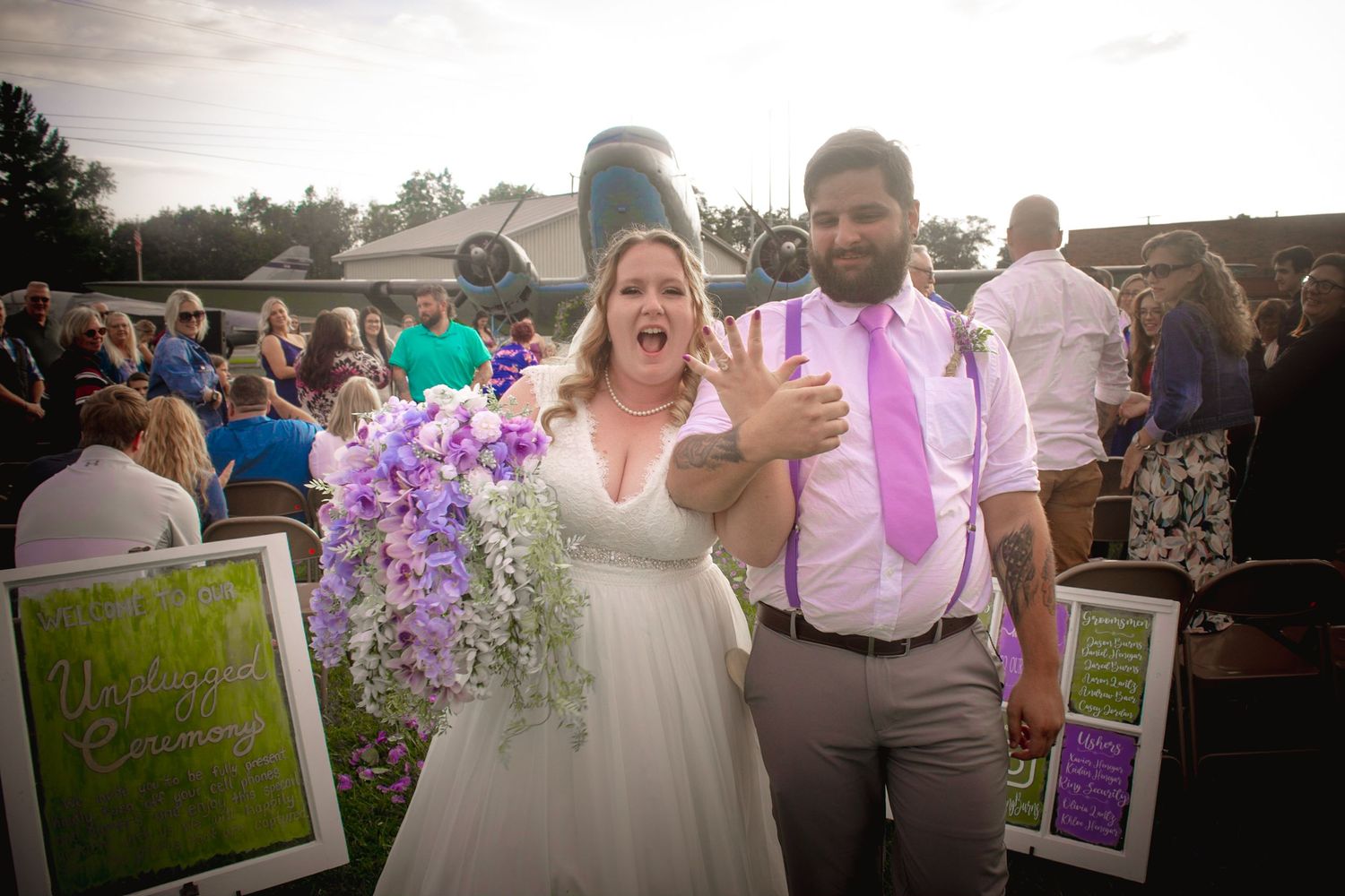 Wedding guests mingle outdoors during a celebration with purple floral decorations.