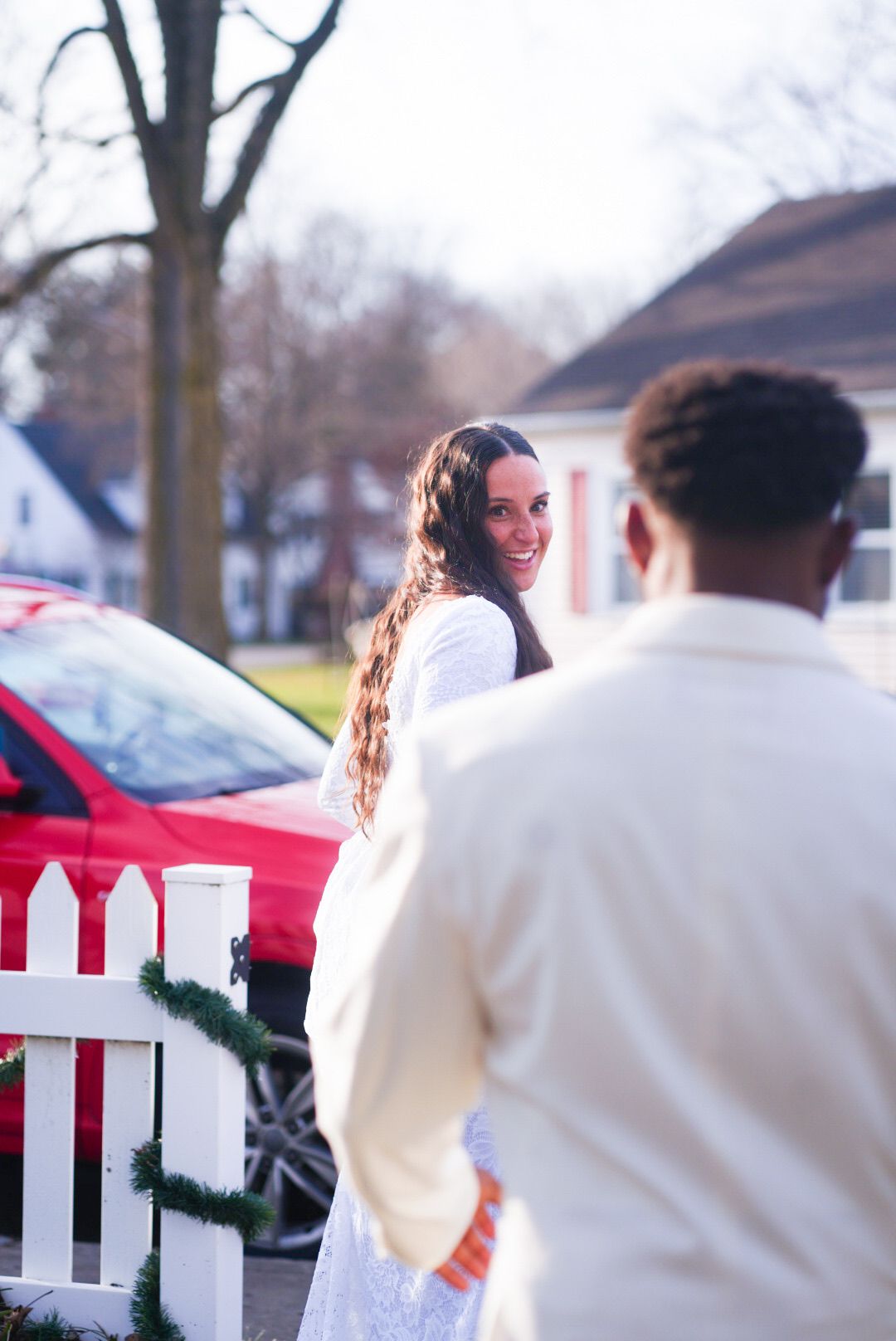 A couple in winter wedding attire share a playful moment by a white picket fence.