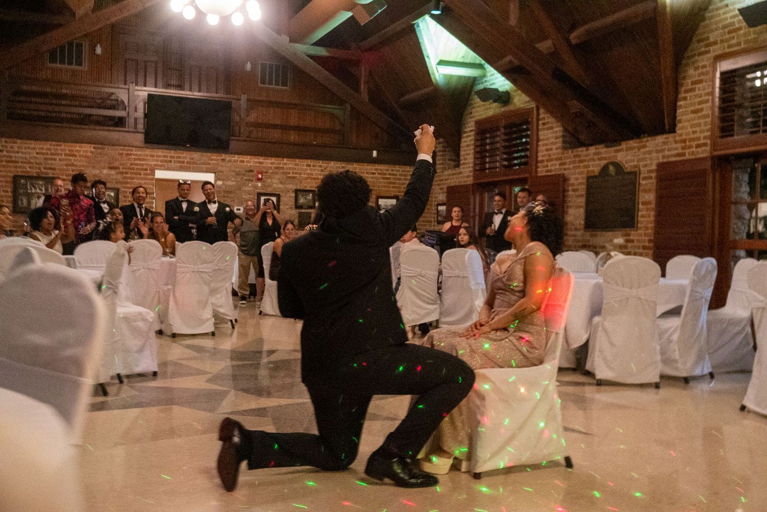 Wedding reception venue with white chair covers and brick walls under ambient lighting.