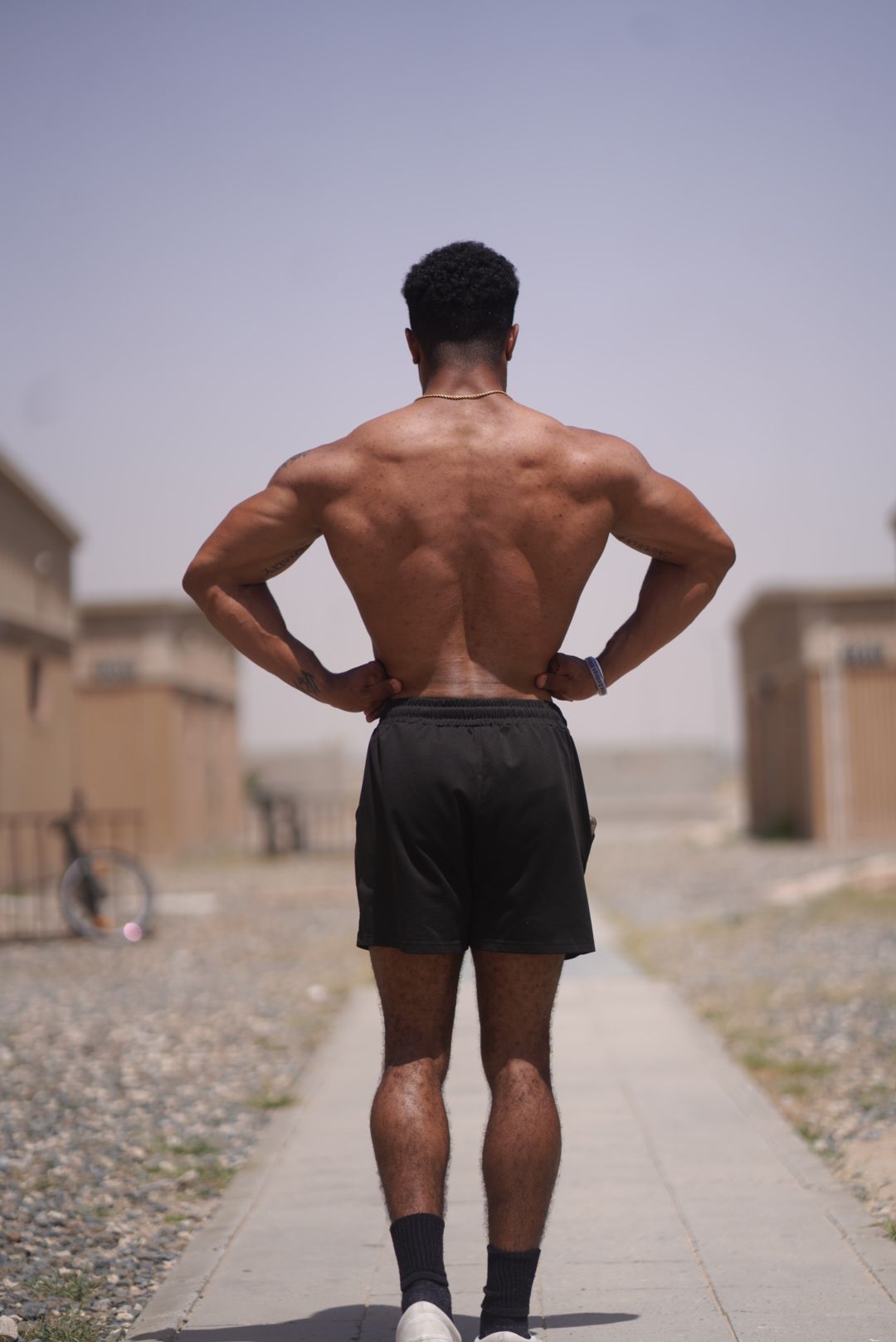 Athletic figure in black shorts walking along a desert pathway.