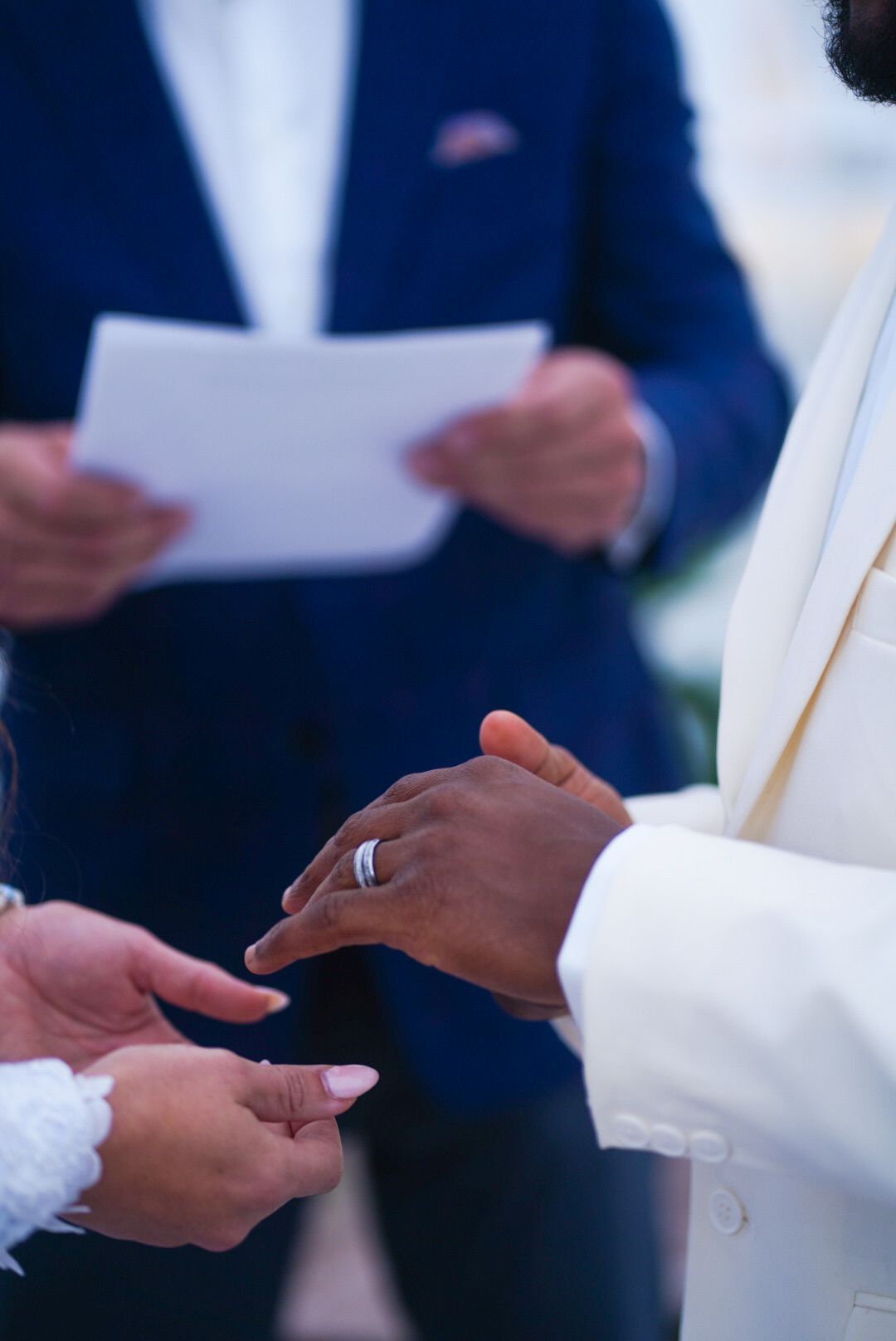 Close-up of hands during ring exchange ceremony with officiant in background.