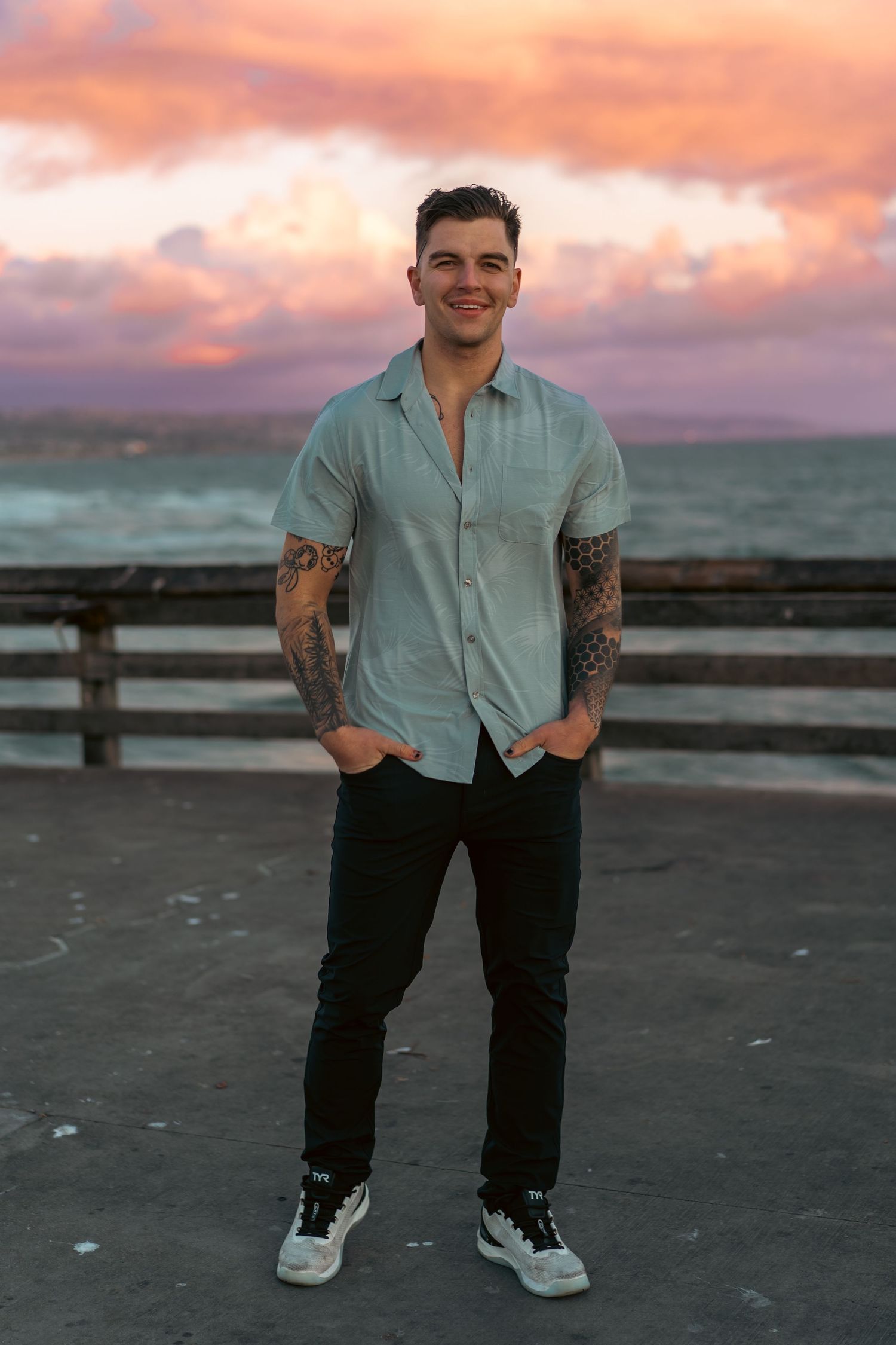 Person in light blue shirt and dark pants standing on pier during vibrant sunset.