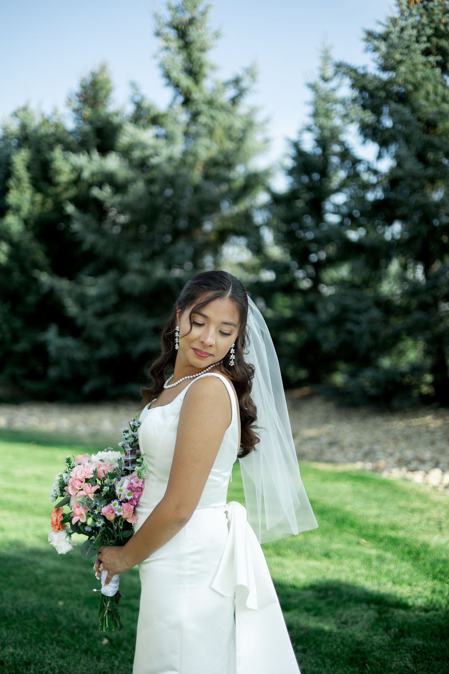 A bridal portrait session in a lush green outdoor setting with soft natural lighting and a white wedding dress.