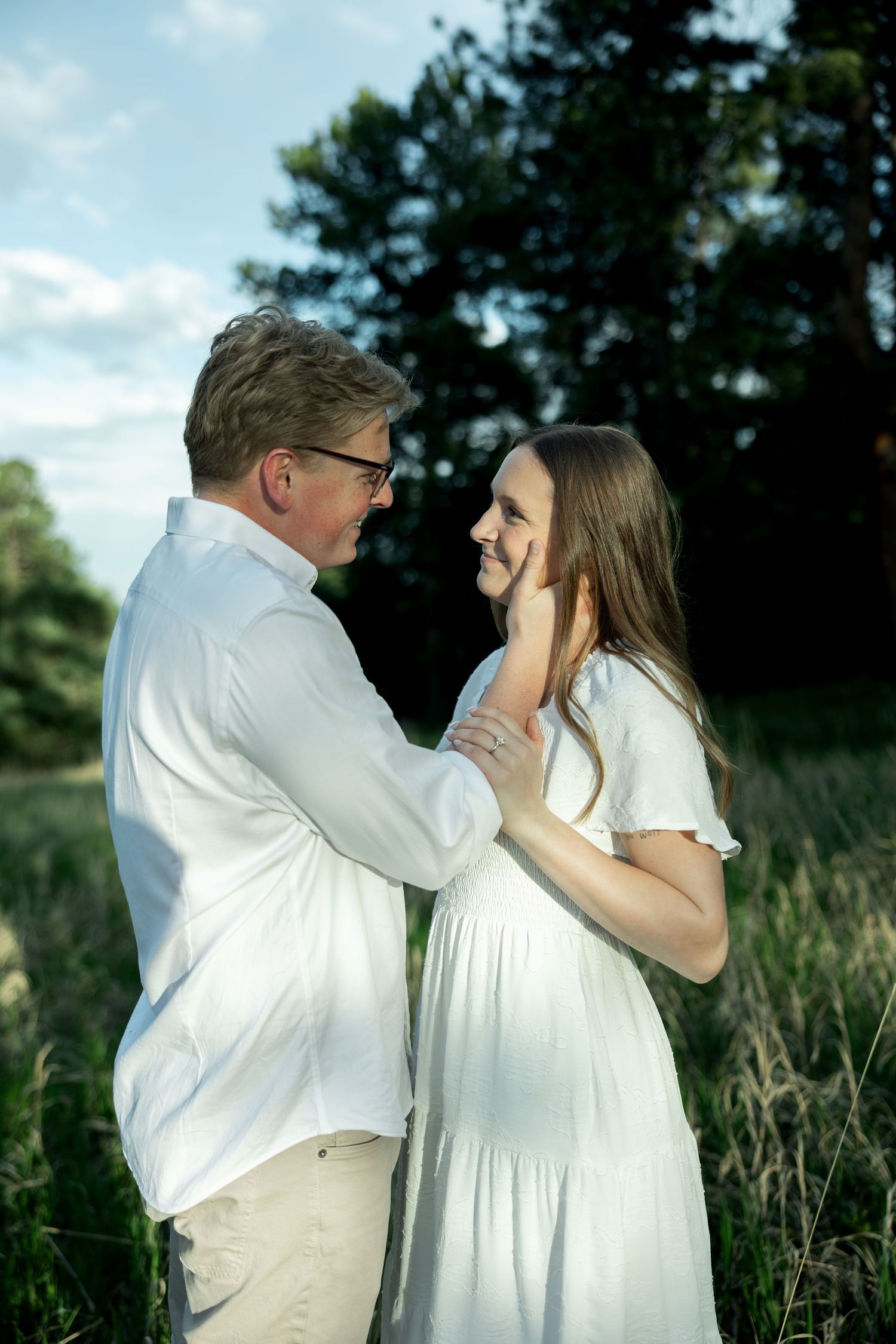 Romantic couple gazing into each others eyes as man gently touches womans face in a sunny outdoor setting.