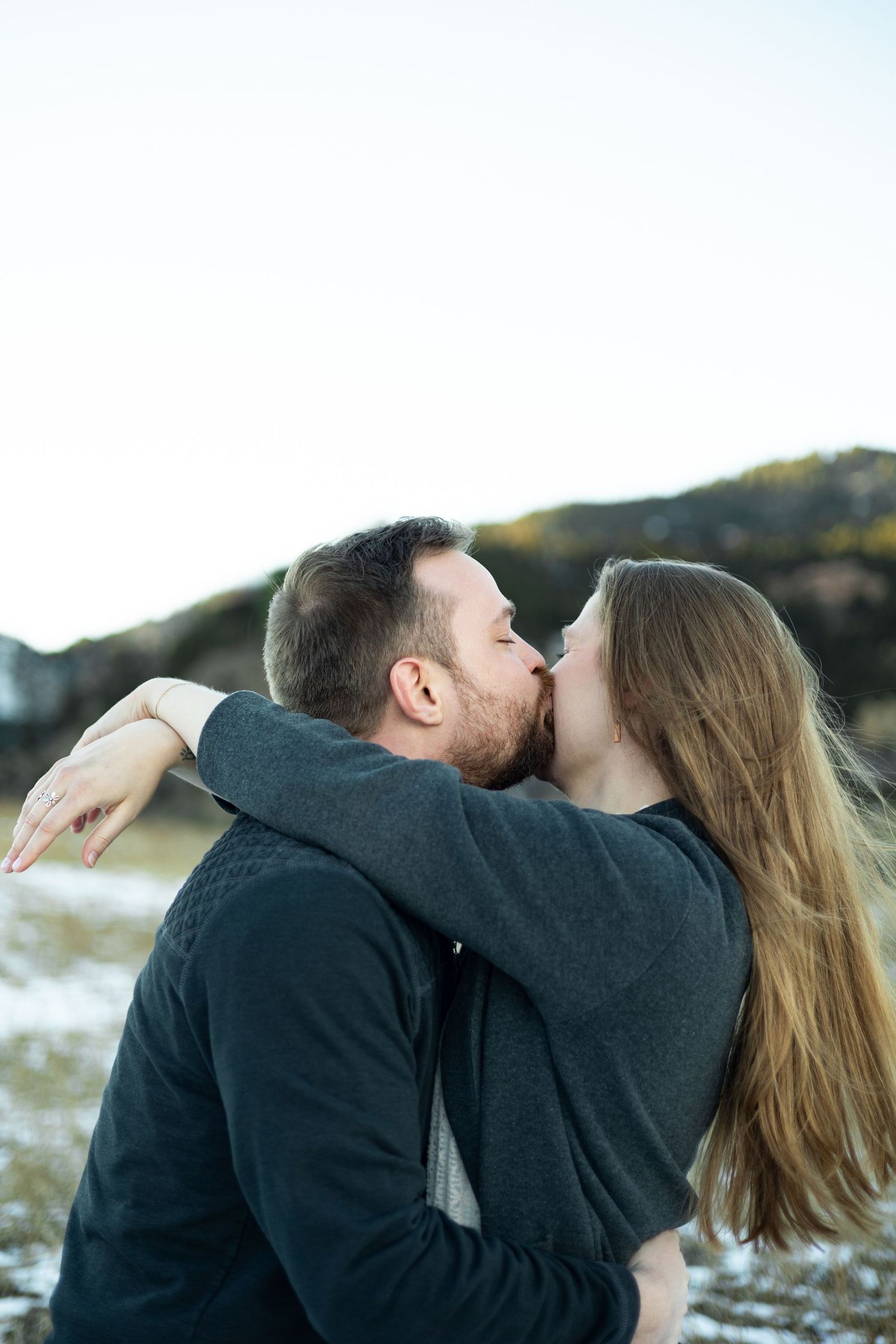 A couple sharing a romantic kiss with mountains in the background at sunset.
