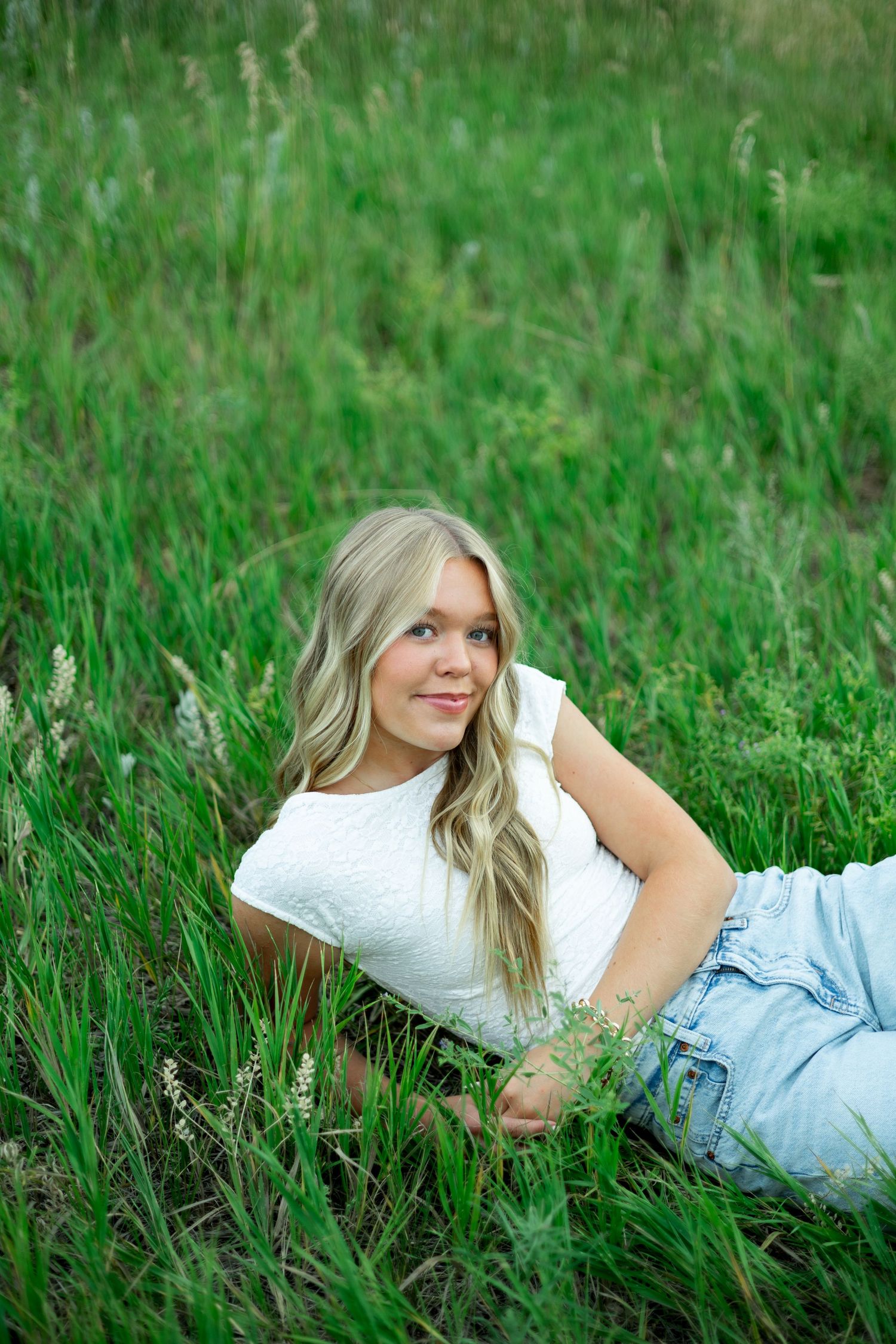 A person in white clothing lies peacefully on bright green grass in a natural outdoor setting.
