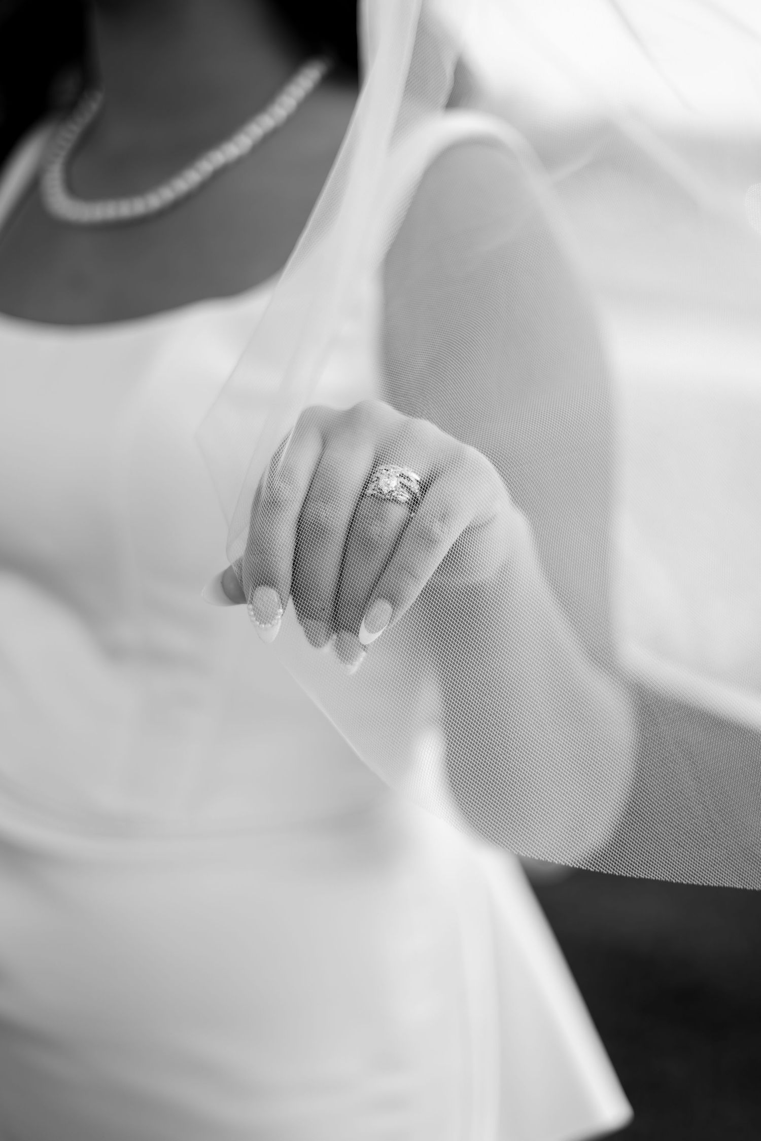 Close-up black and white detail of someone's hands wearing an elegant engagement ring.